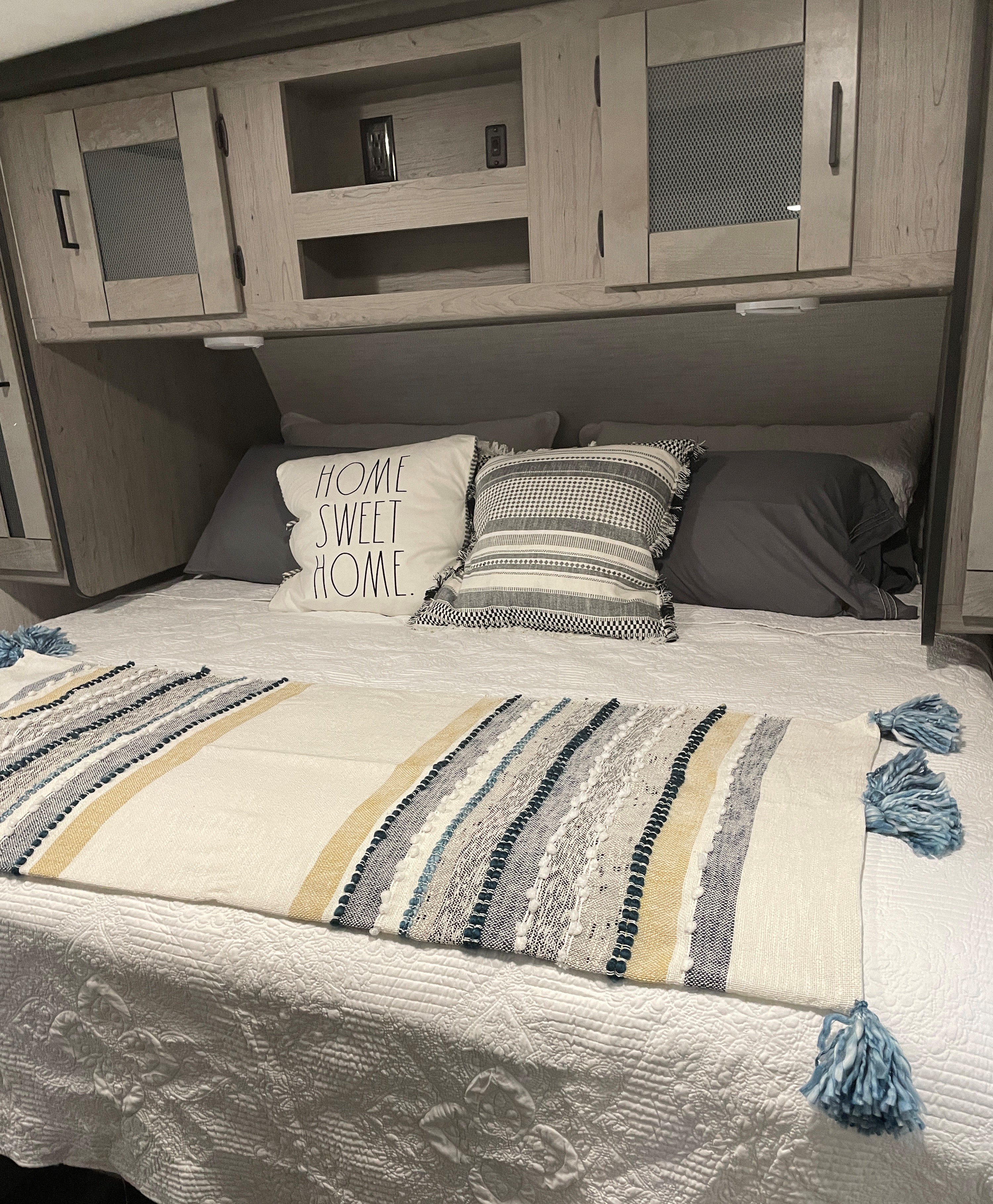 Cozy rv rental bedroom setup: quilted bed, 'Home Sweet Home' pillow, striped runner, and functional overhead cabinets.. Heartland RVs Mallard 2021