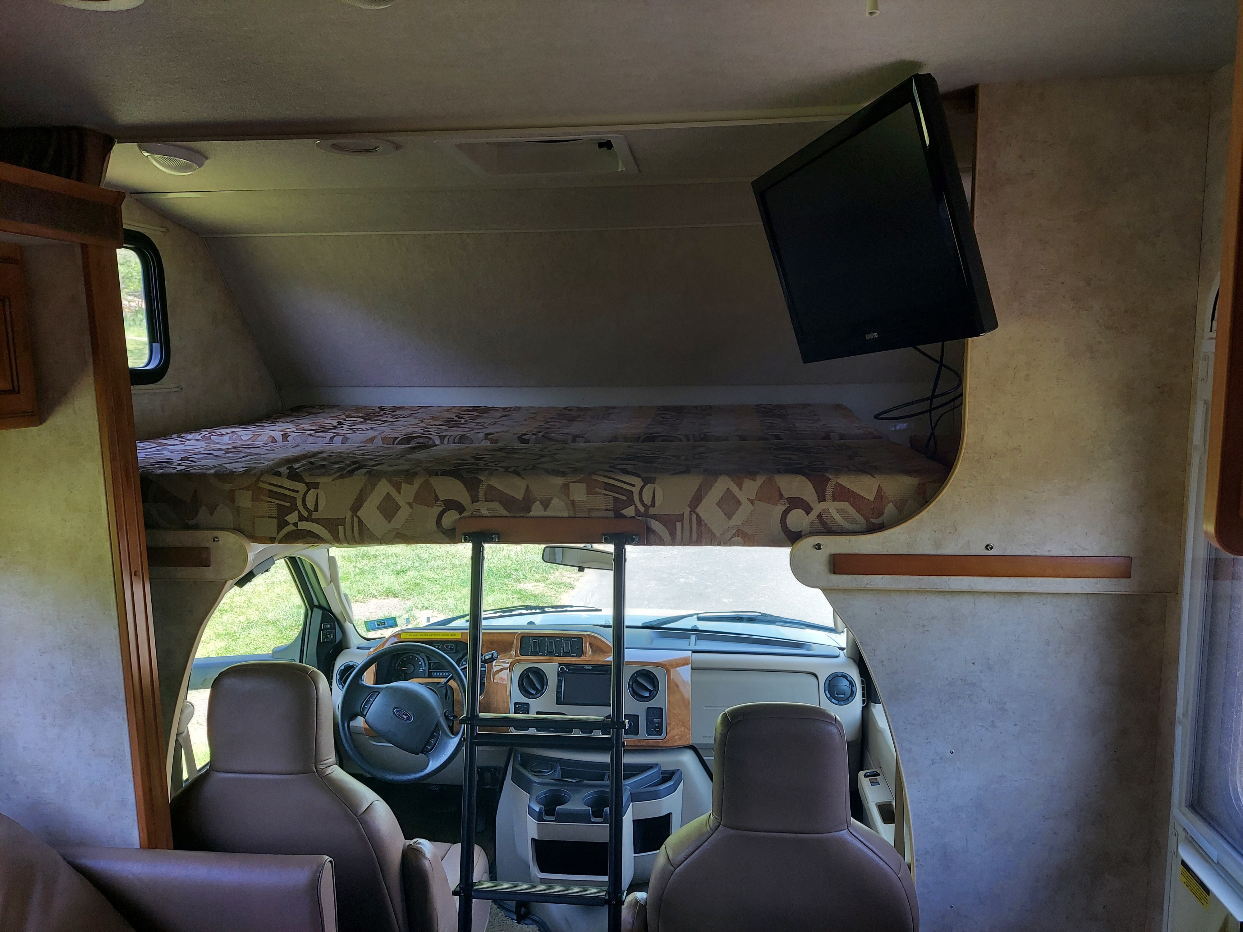 View of an RV rental's interior, highlighting the overhead bunk with ladder, driver's cockpit, and mounted TV.. Winnebago Access 2011