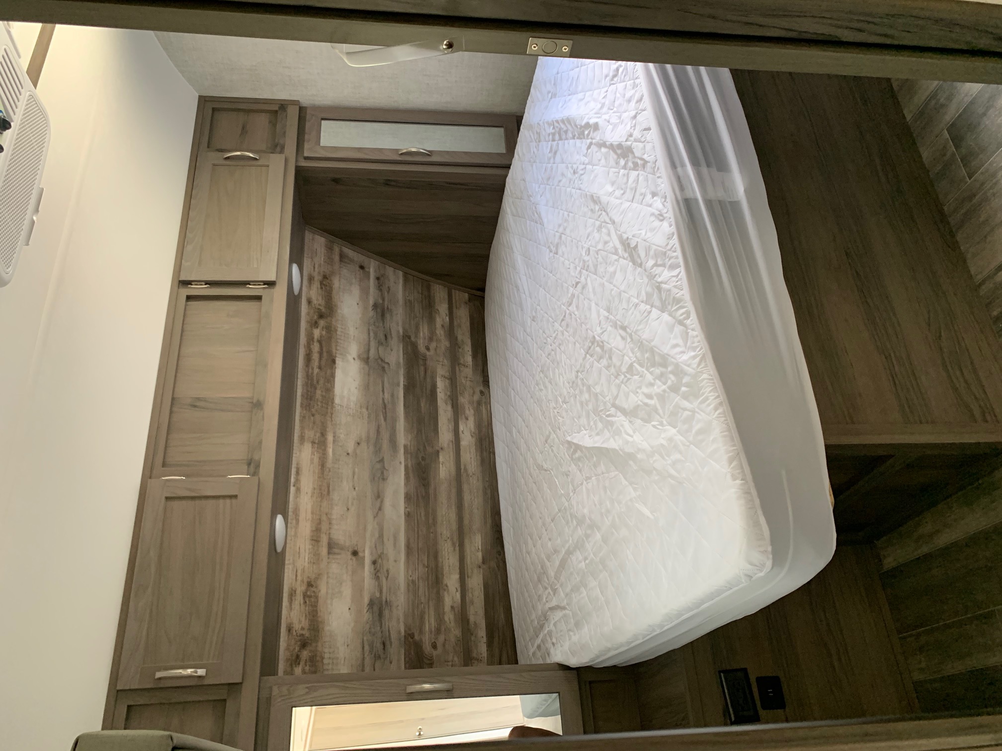 Inside a modern RV rental bedroom: white bed, wood-look walls & built-in storage. Compact comfort.. Gulf Stream Envision 2021