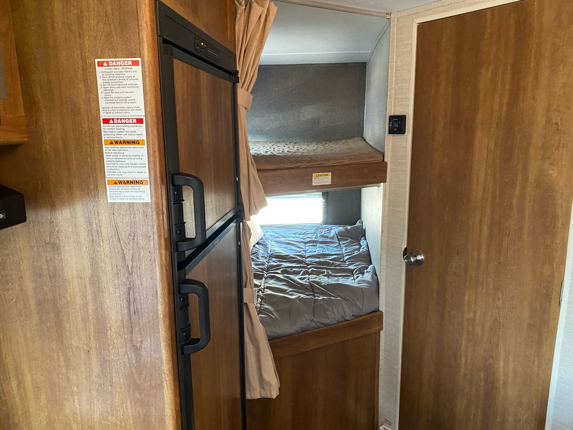 RV rental interior featuring bunk beds, a refrigerator, and essential safety labels for propane and gas appliances.. Keystone Springdale 2016