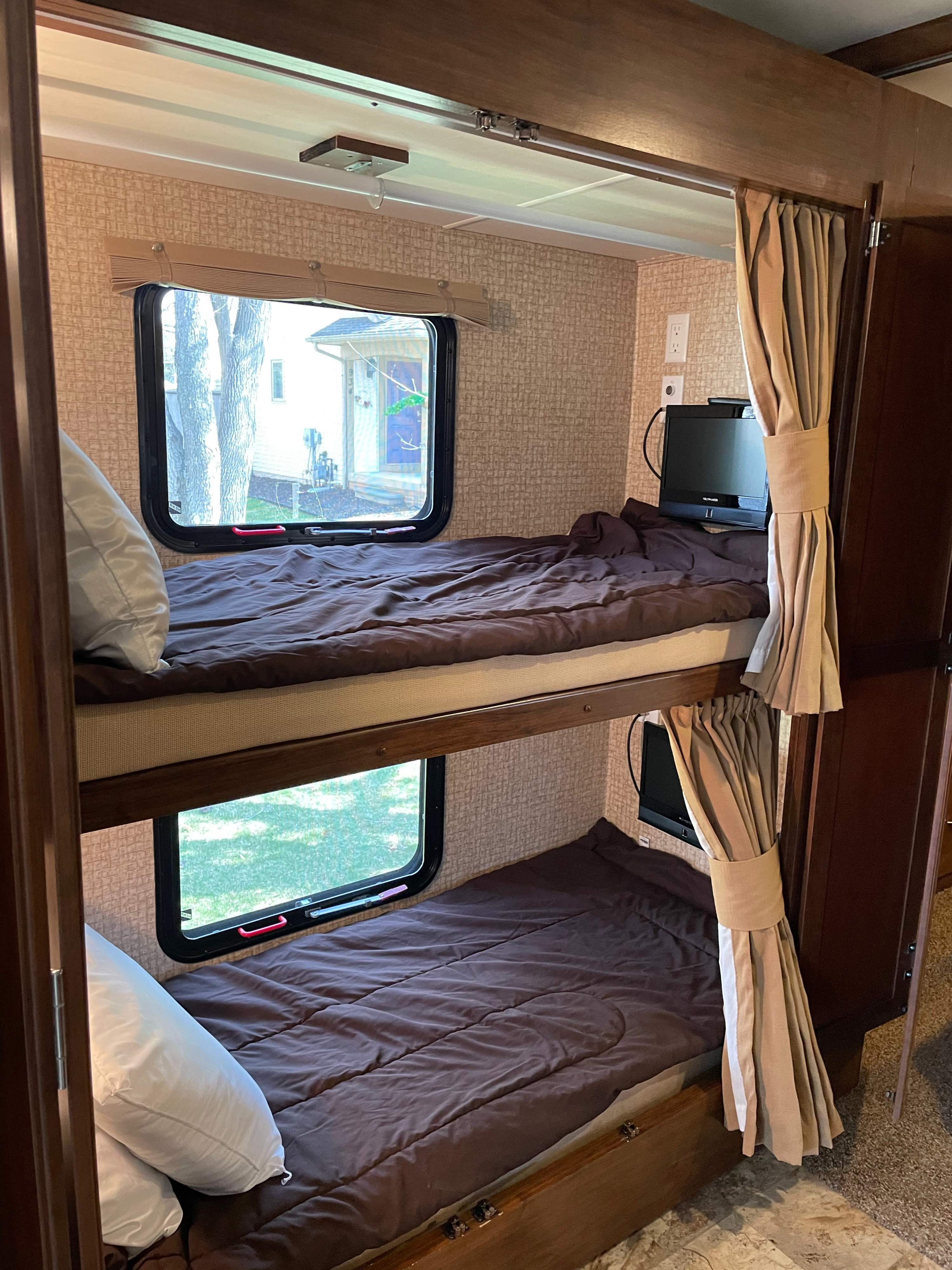 Two stacked bunk beds with brown bedding, pillows, windows, and TVs inside a compact RV rental, perfect for travel.. Coachmen Mirada 35BH 2016