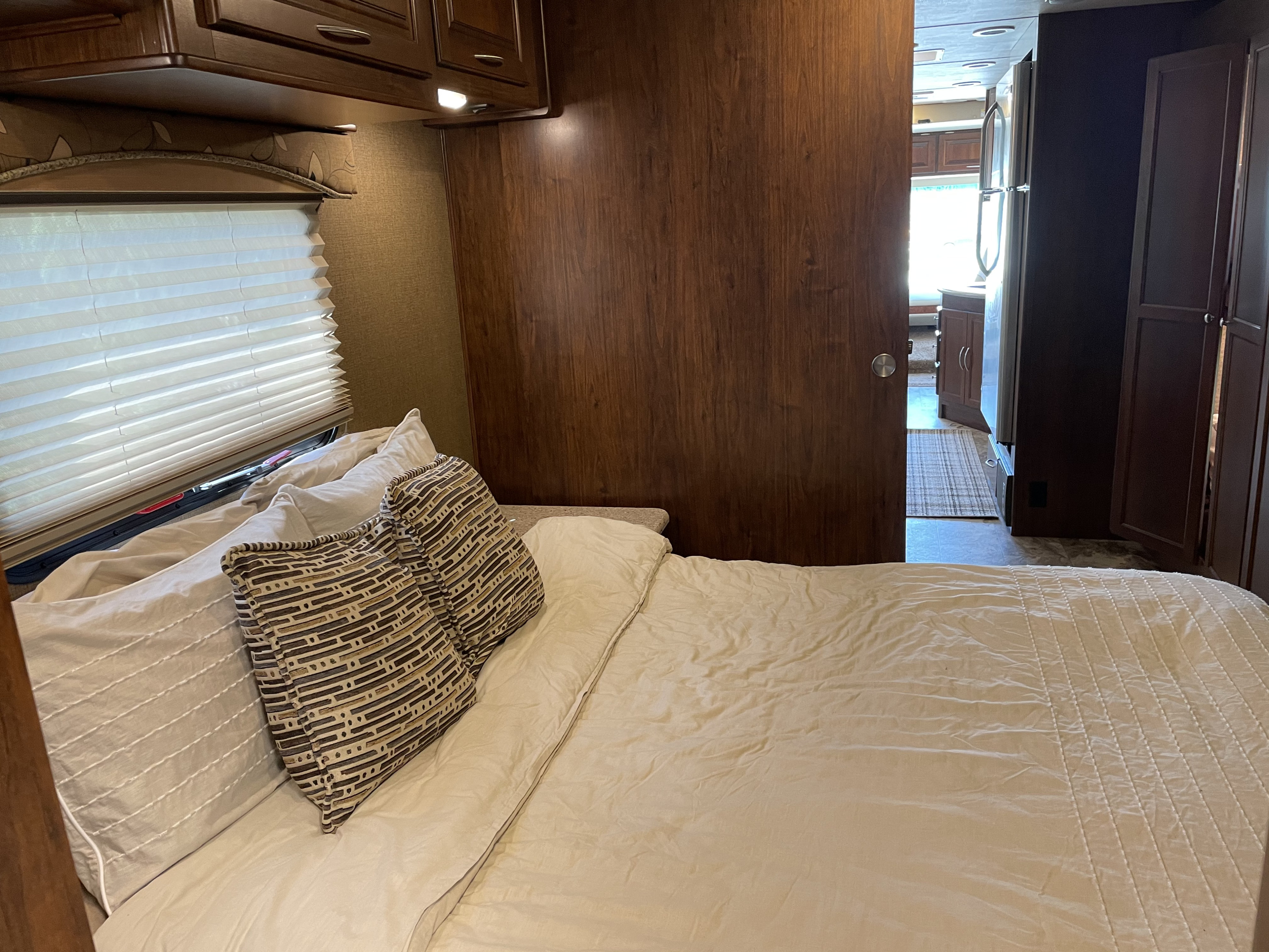 RV rental: Inside a comfortable bedroom with a window, viewing the spacious kitchen and living area through a wooden sliding. Coachmen Mirada 35BH 2016