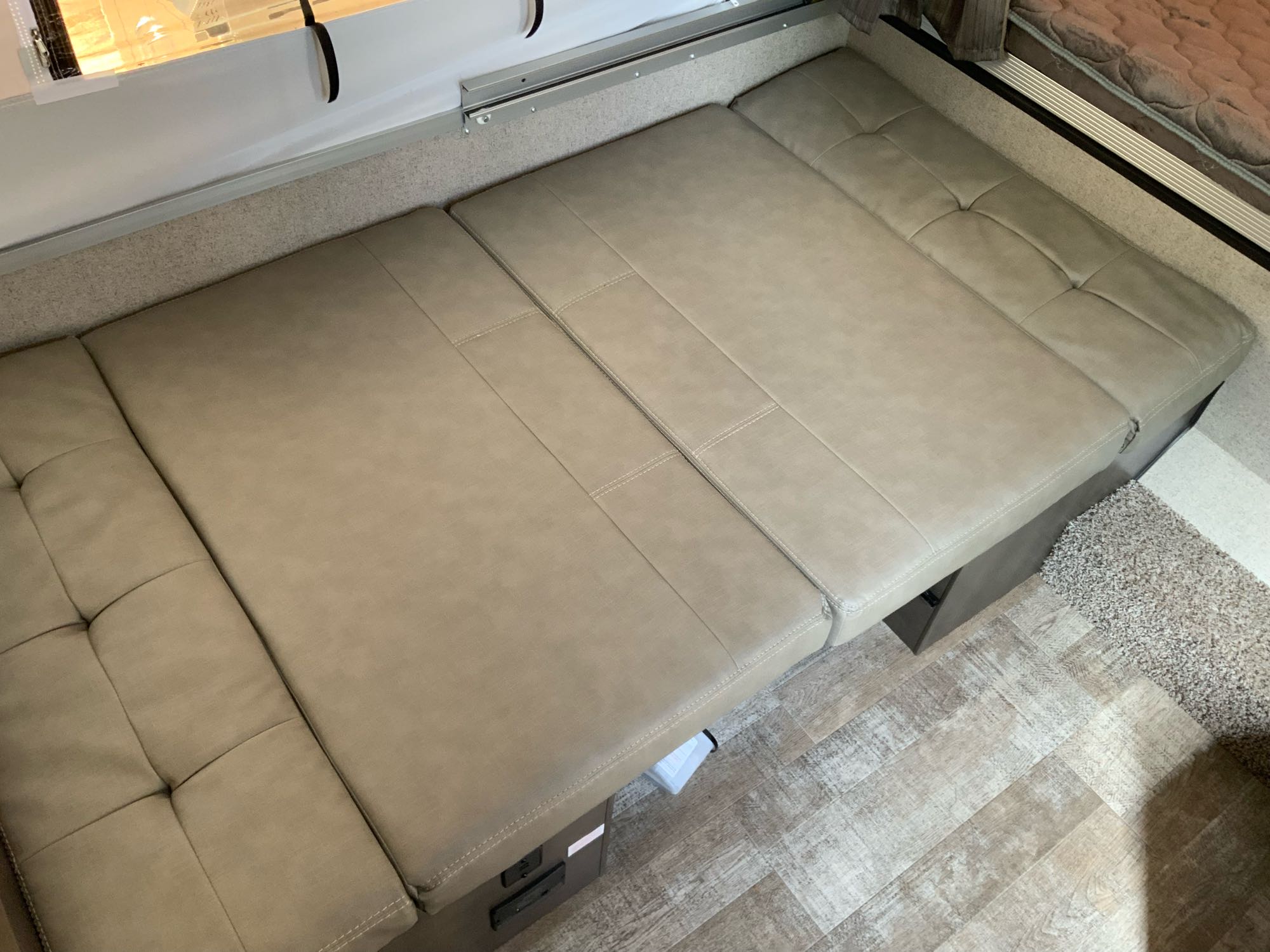 RV rental interior featuring a beige convertible bench seat and bed, with light wood-look and carpet flooring.. Forest River Rockwood Lite 2020