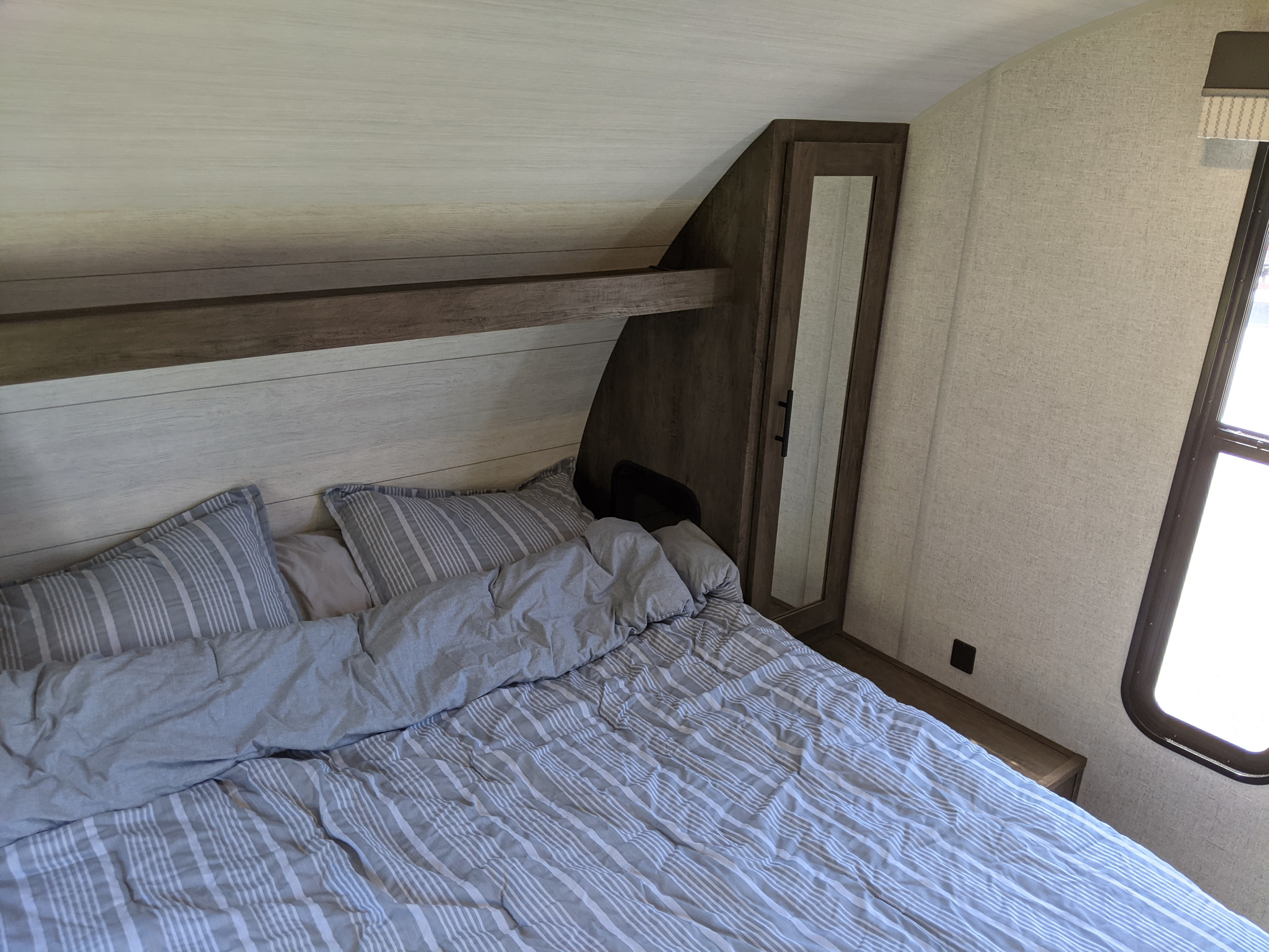 Cozy RV rental bedroom with striped bedding, built-in shelving, mirror, and window. Ideal travel space.. Forest River Wildwood X-Lite 2021
