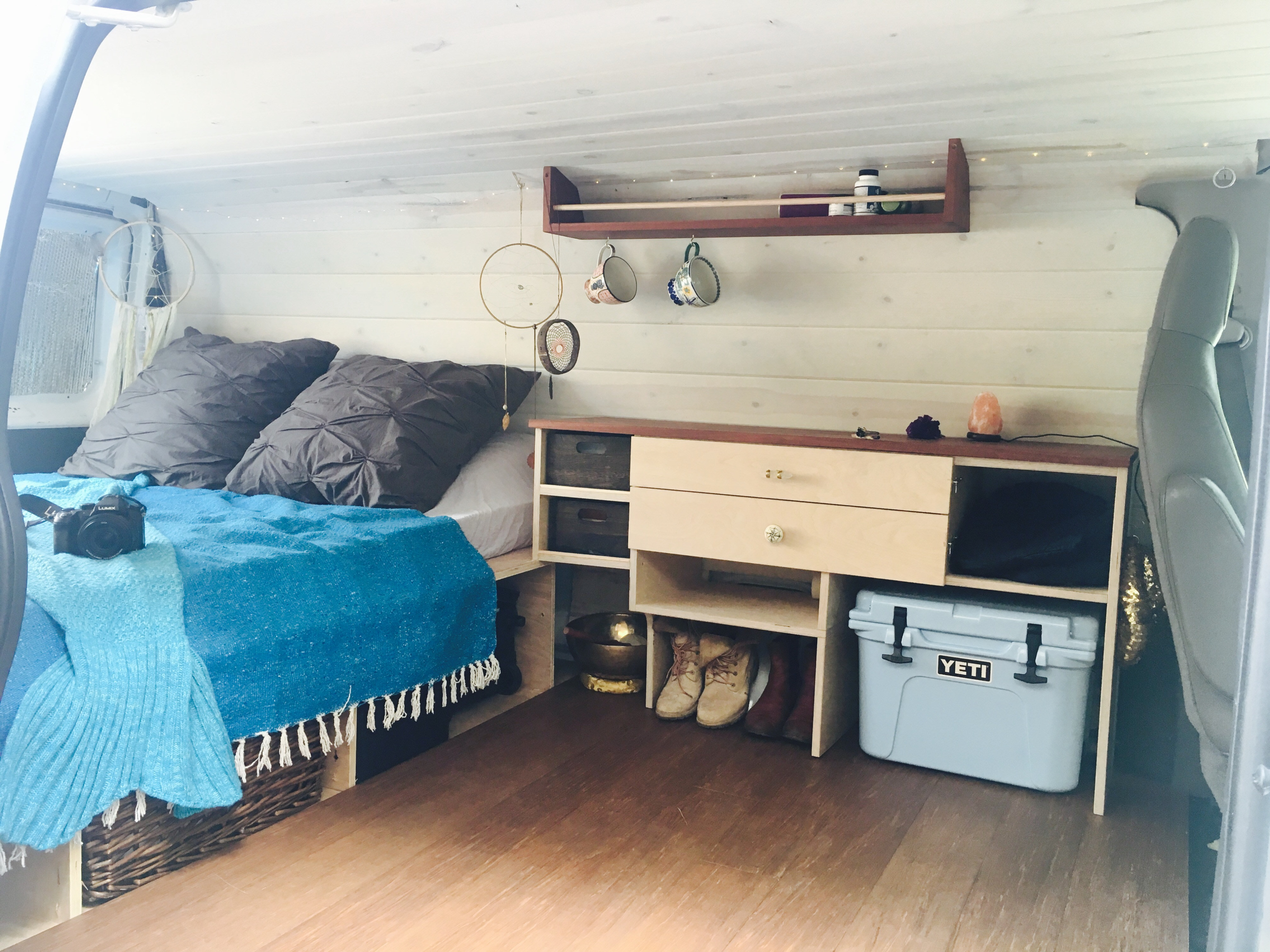 Cozy RV rental interior with bed, custom storage, Yeti cooler, and hanging mugs. Ideal for compact van life travel.. Ford Ford E350 2011