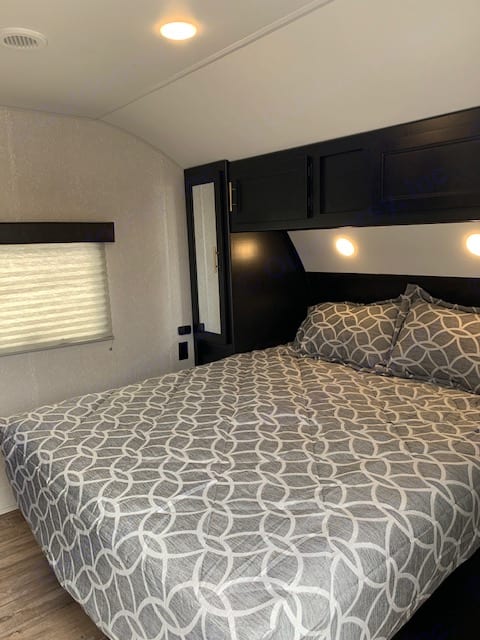 Experience comfort in this RV rental bedroom: patterned bed, overhead storage, and soft lighting. Ready for your next adventure!. Forest River Cherokee Grey Wolf 2021