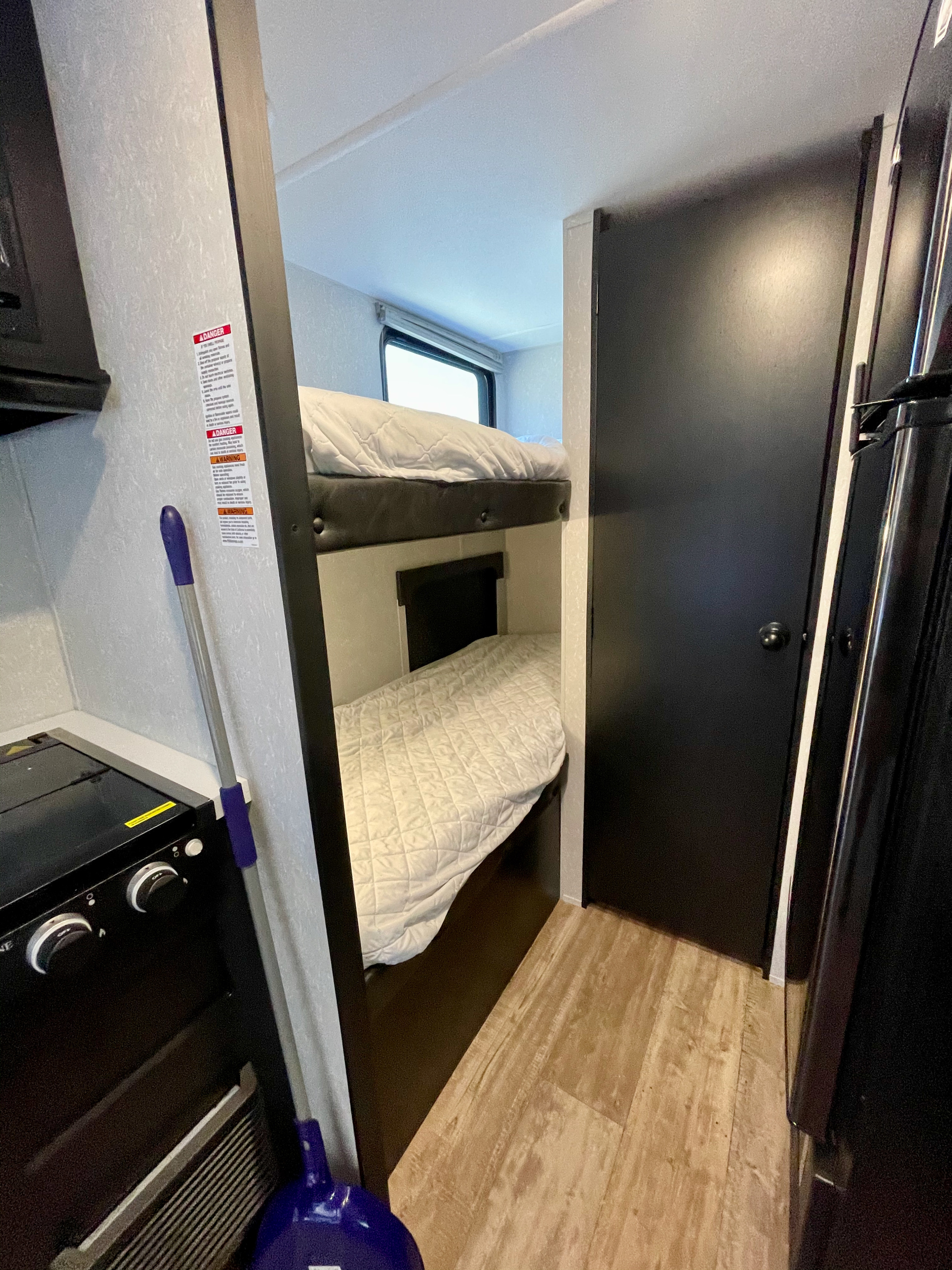 Cozy RV rental interior: bunk beds with white bedding, a stove, and a dark door. Perfect for family adventures.. Forest River Cherokee Wolf Pup 2021