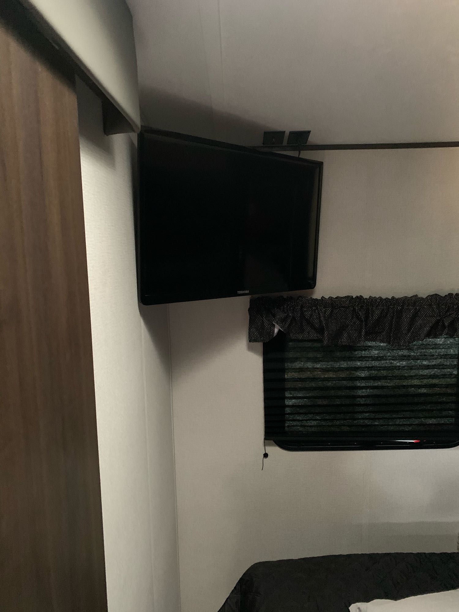 An RV rental bedroom featuring a wall-mounted TV, window blinds, and dark bedding, providing a functional space.. Keystone Springdale 2021