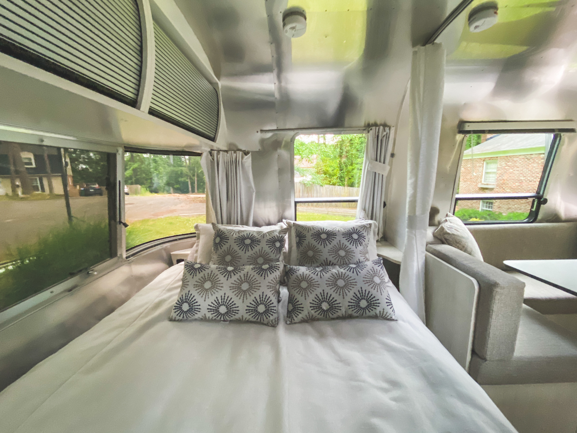 Inside a stylish rv rental: a comfy bedroom with pillows, metallic walls, & window views. Perfect for travel!. Airstream Other 2021