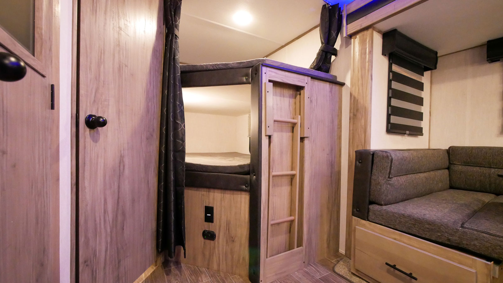 RV rental interior: Cozy bunk beds with ladder and comfortable sofa seating, ideal for family trips.. Forest River Alpha Wolf 26DBH-L 2021
