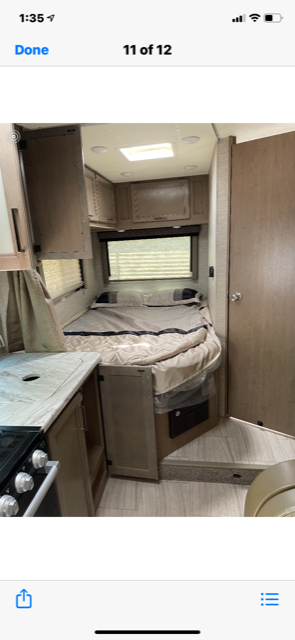 Cozy RV rental interior: a neatly made bed, overhead cabinets, window, and glimpse of the kitchen counter.. Thor Motor Coach Coleman 2021