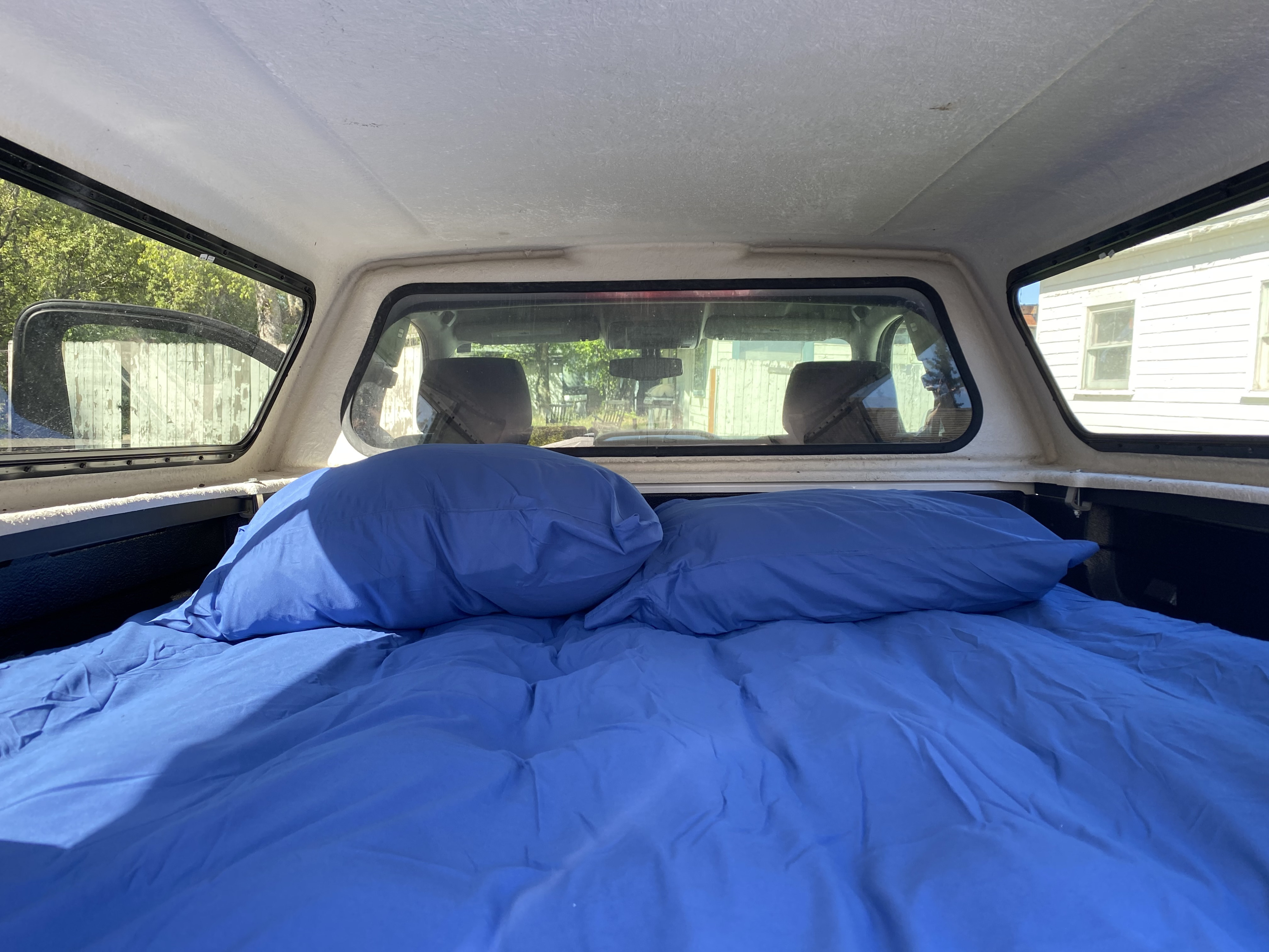 Blue bedding fills a truck bed camper, offering a cozy sleep setup. Perfect for an rv rental adventure!. Chevrolet Silverado 2015