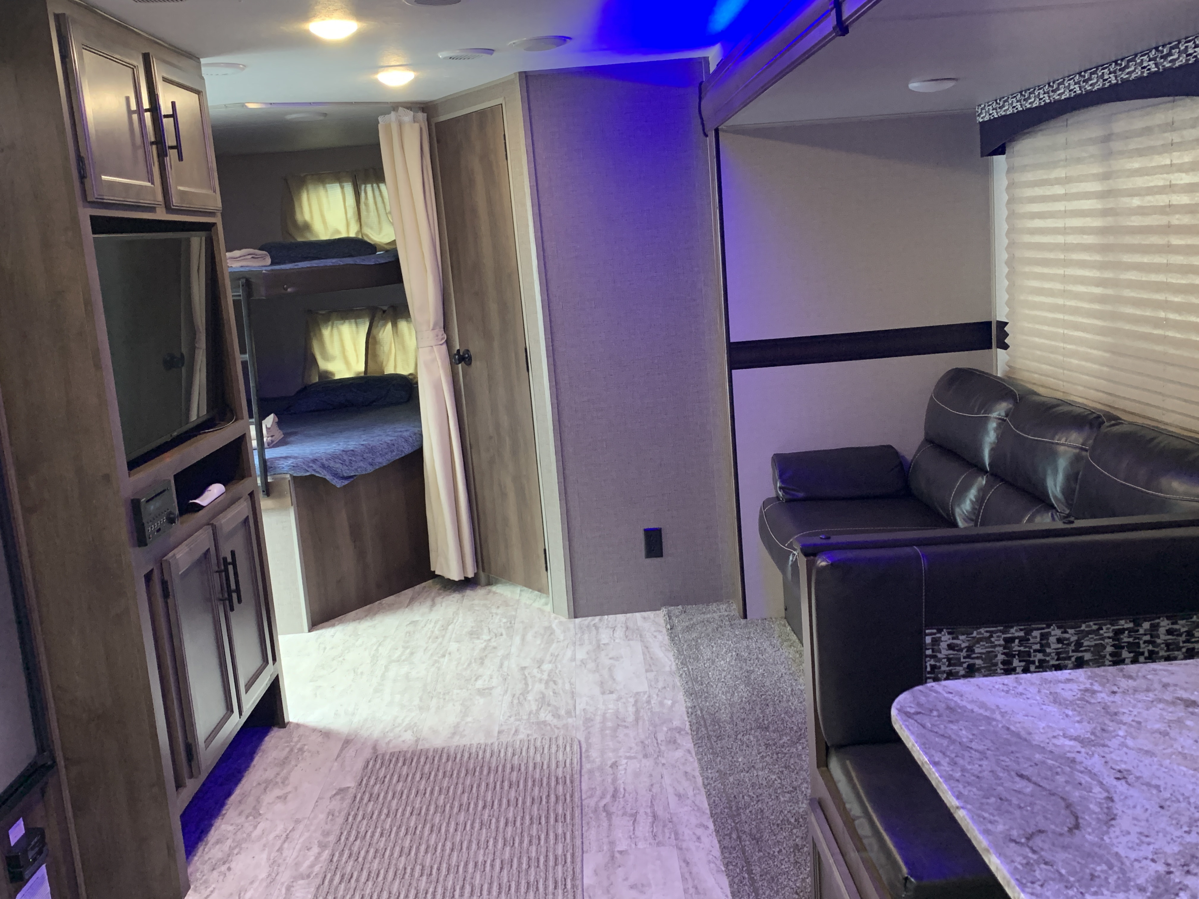 RV rental interior showing living area with sofa, dining booth, and bunk beds. Blue accent lighting creates a cozy atmosphere.. K-Z Manufacturing Connect 2018