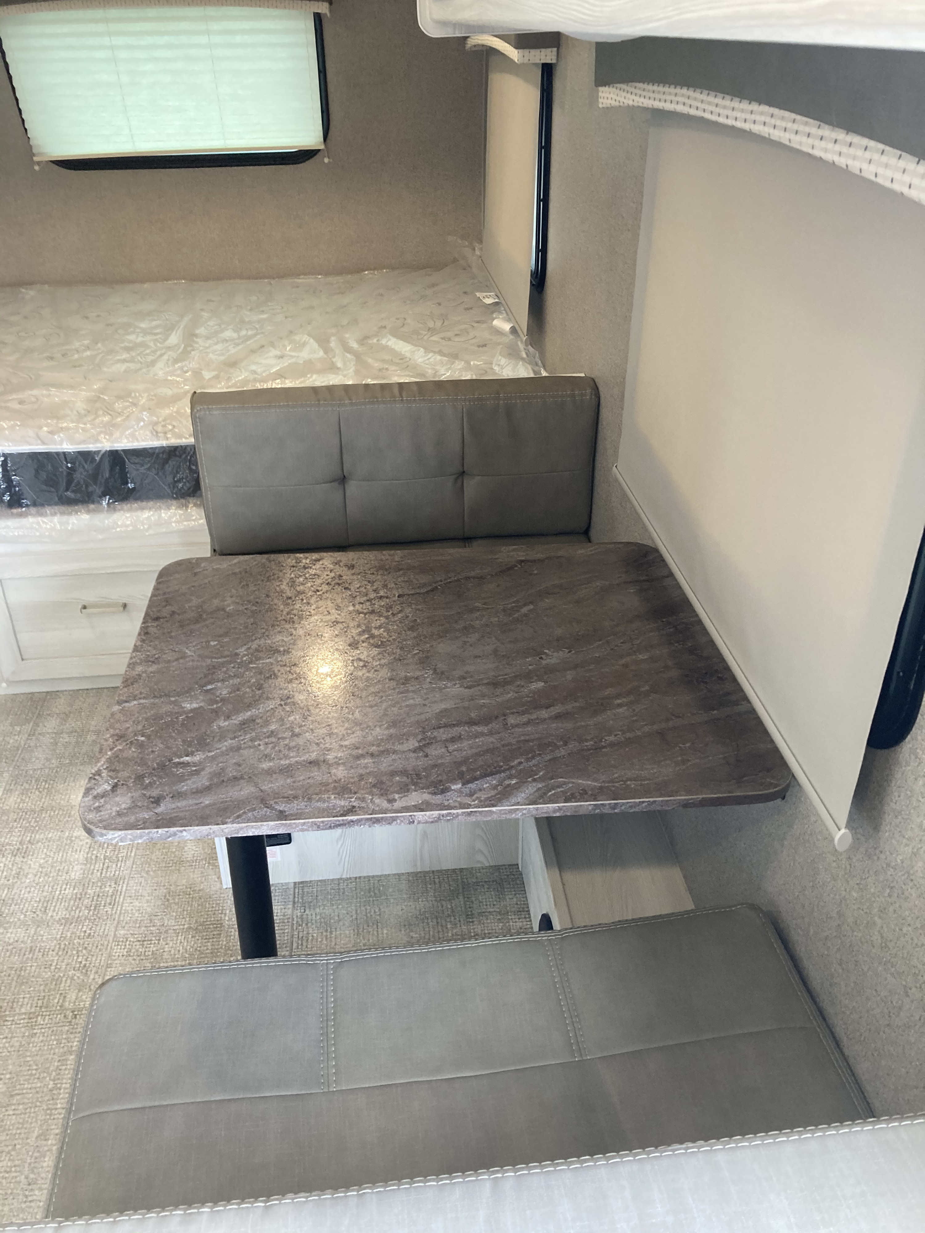 Modern RV rental interior: A spacious dinette with grey benches, a speckled table, and a bed in the background.. geo pro G19QB 2020