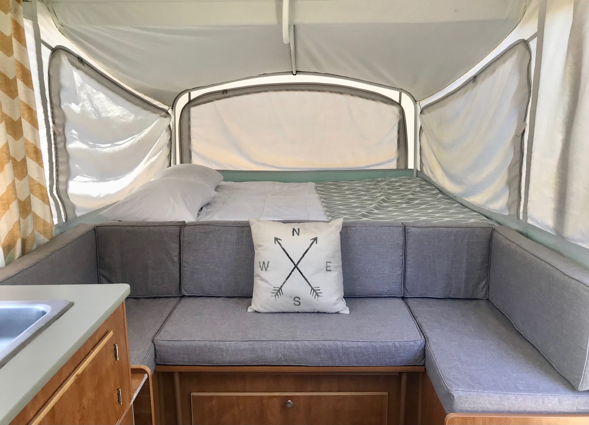 Cozy pop-up RV rental interior featuring a comfortable bed, gray cushioned seating, and a small kitchen sink.. Fleetwood Sea Pine 2006