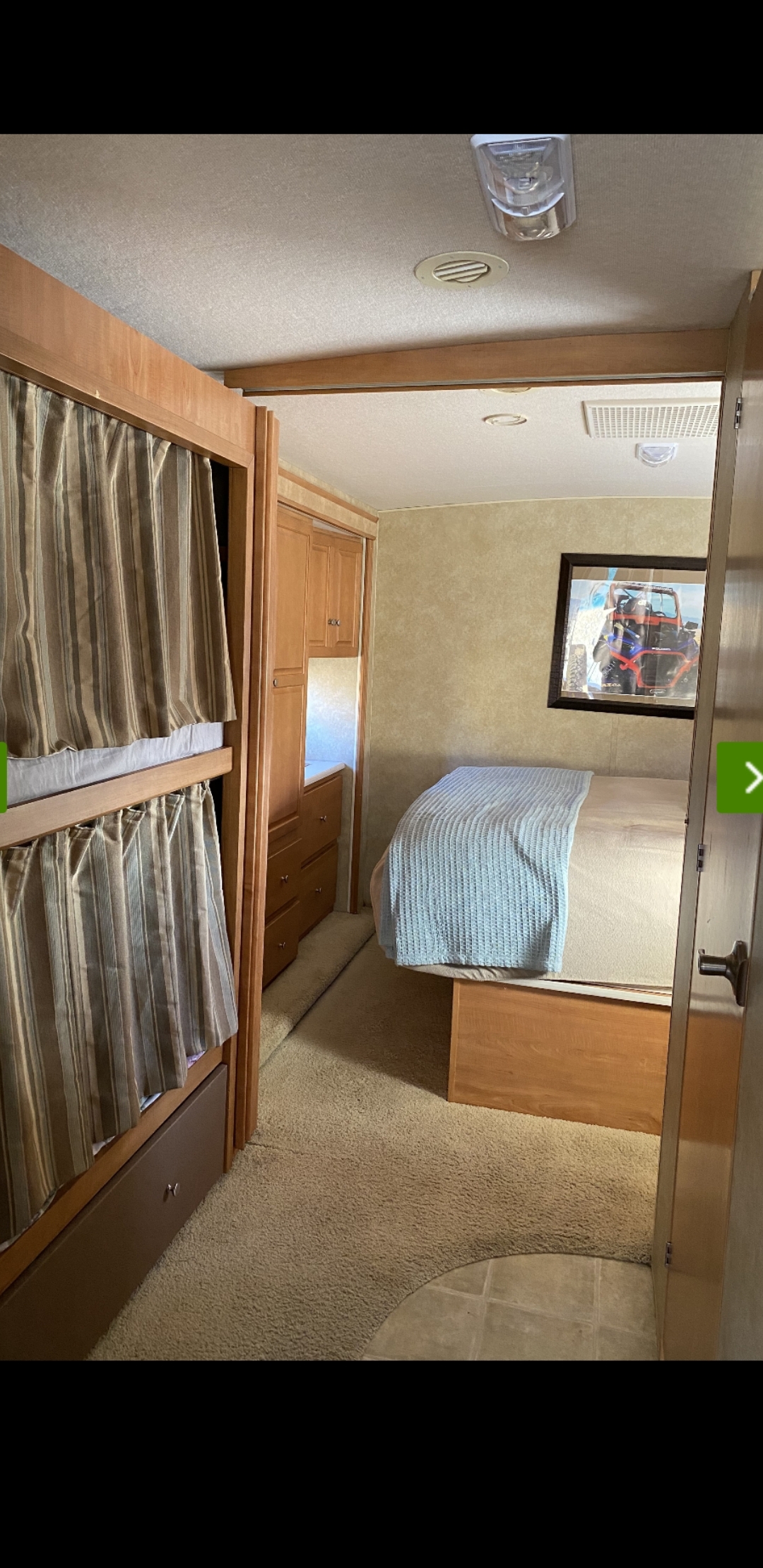 Inside this RV rental: Left has bunk beds with curtains; right, a private bedroom with a made bed, dresser, and wall art. Carpeted floor.. Winnebago Vista 2009