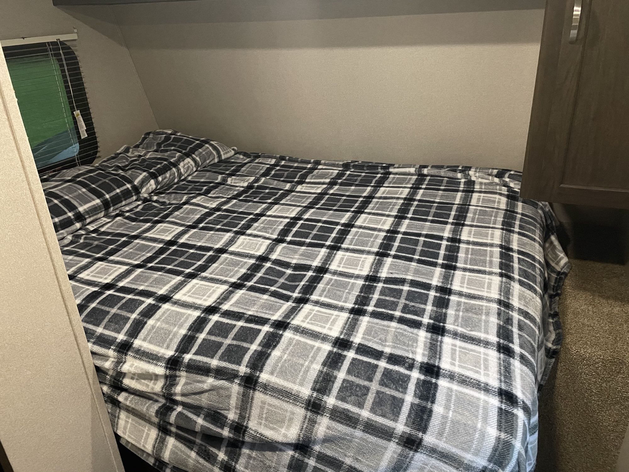 Comfortable plaid bed in an RV rental bedroom, featuring a window and built-in storage.. Keystone Springdale 2018