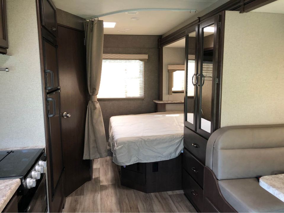 Inside an RV rental: a modern interior featuring a cozy bedroom, compact kitchen, and inviting dinette, all in neutral tones.. Thor Motor Coach Freedom Elite 2021