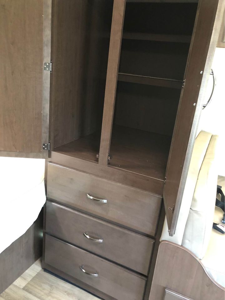 RV rental: Dark wood cabinet with opened wardrobe doors revealing shelves, and three dresser drawers below, for essential storage.. Thor Motor Coach Freedom Elite 2021