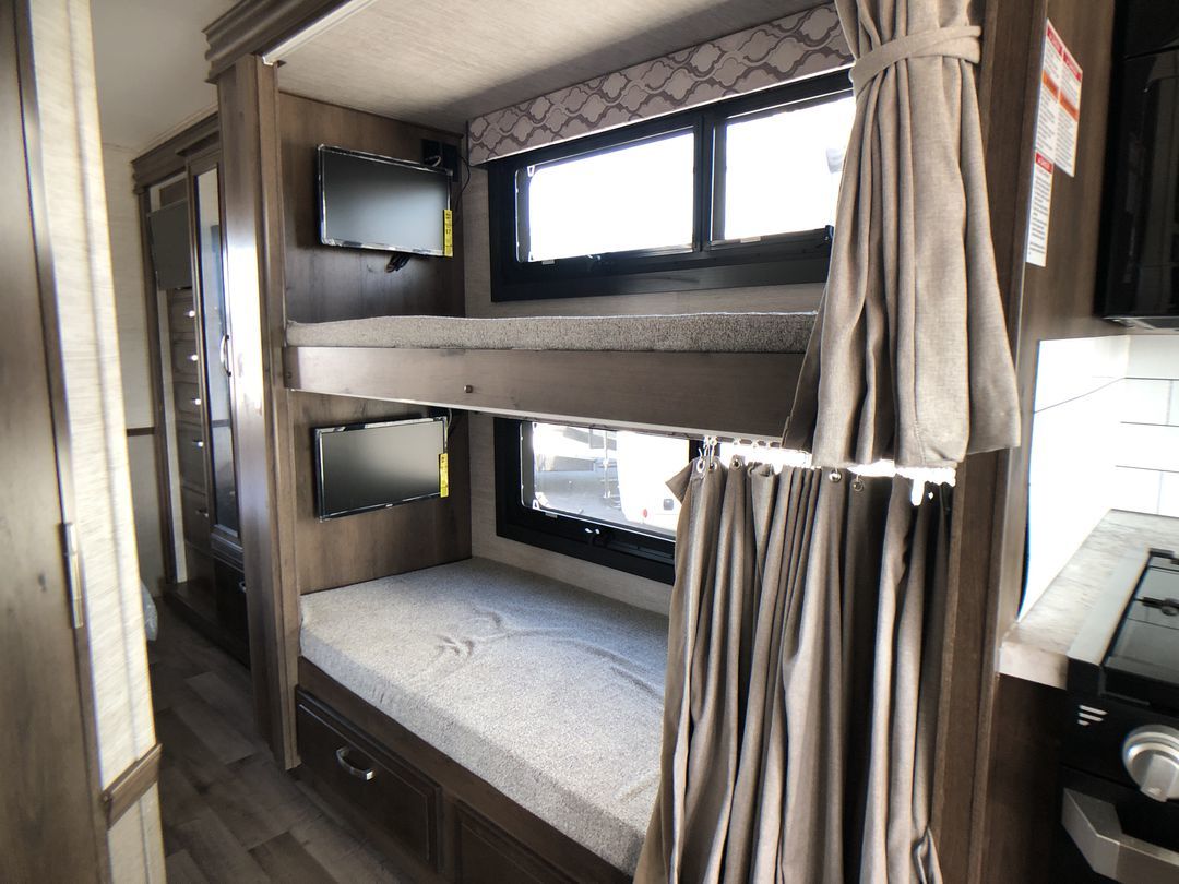Modern RV rental interior with bunk beds, each featuring a TV, and a nearby wardrobe. Ideal for family adventures.. Jayco Alante 2021