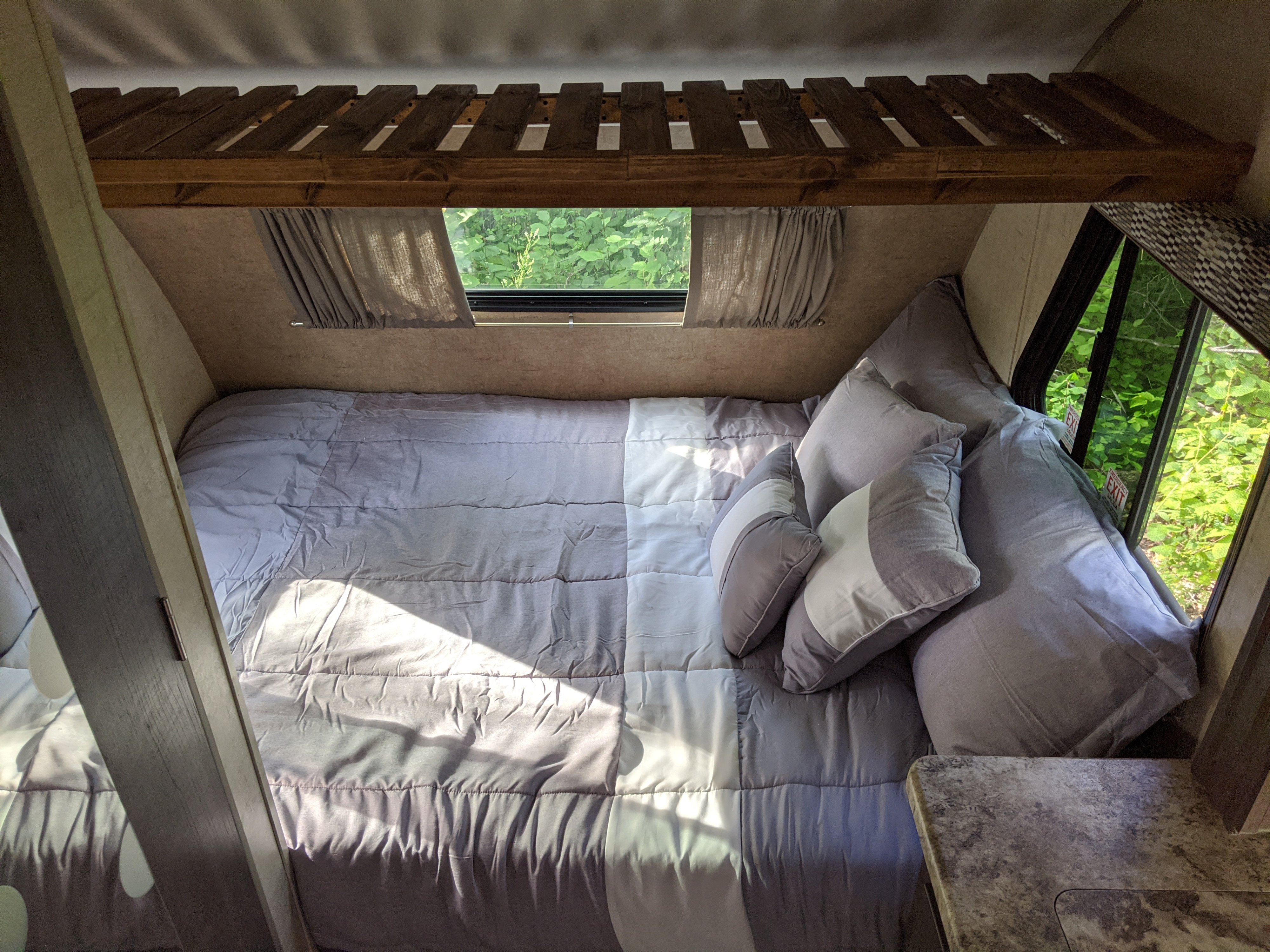 Cozy RV rental bedroom: two-tone bedding, soft pillows, overhead bunk, and windows revealing a green forest.. Forest River R-Pod 178 2017