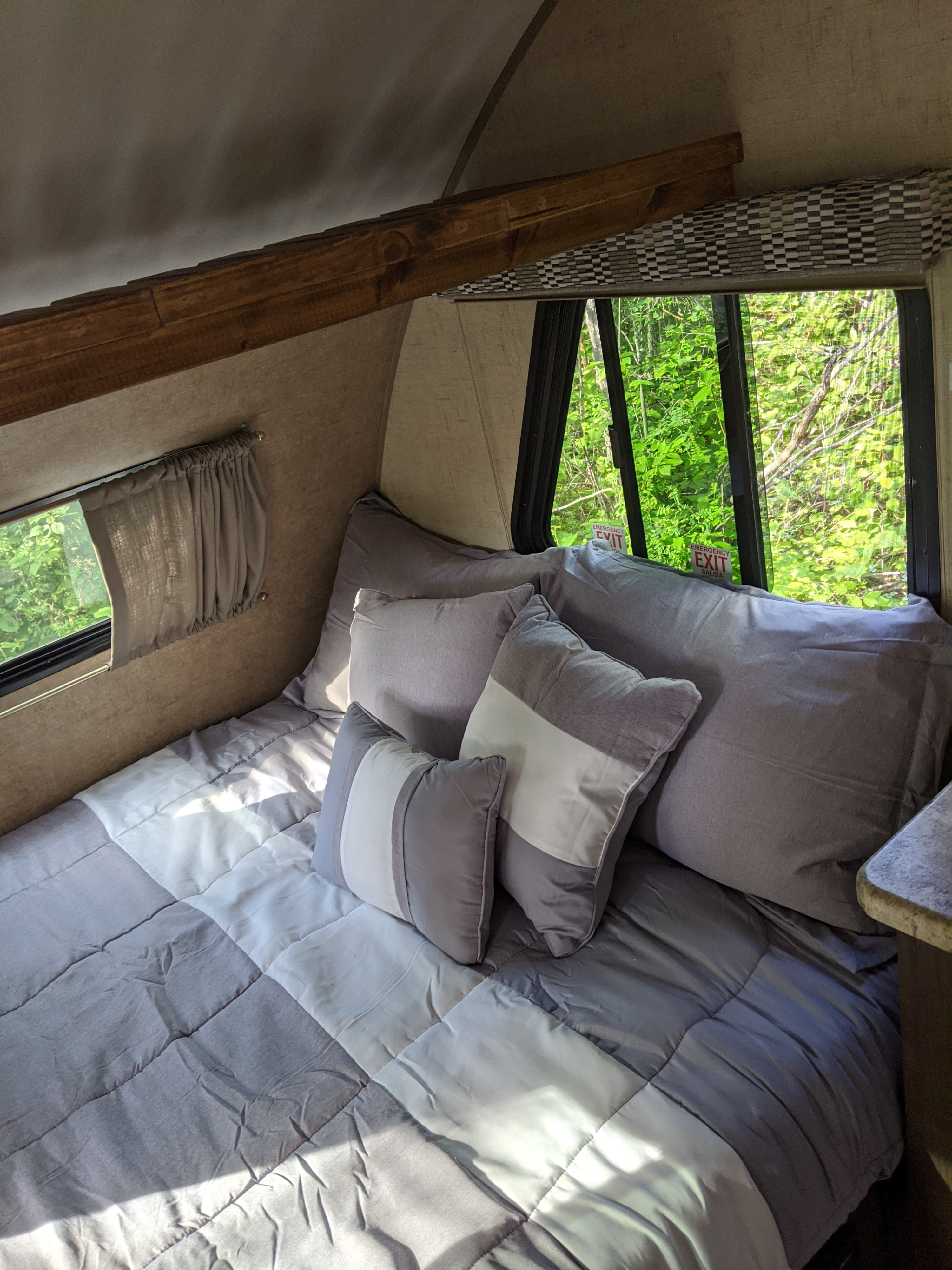 Cozy RV rental bedroom with comfortable grey and white bedding and large windows revealing green nature outside.. Forest River R-Pod 178 2017
