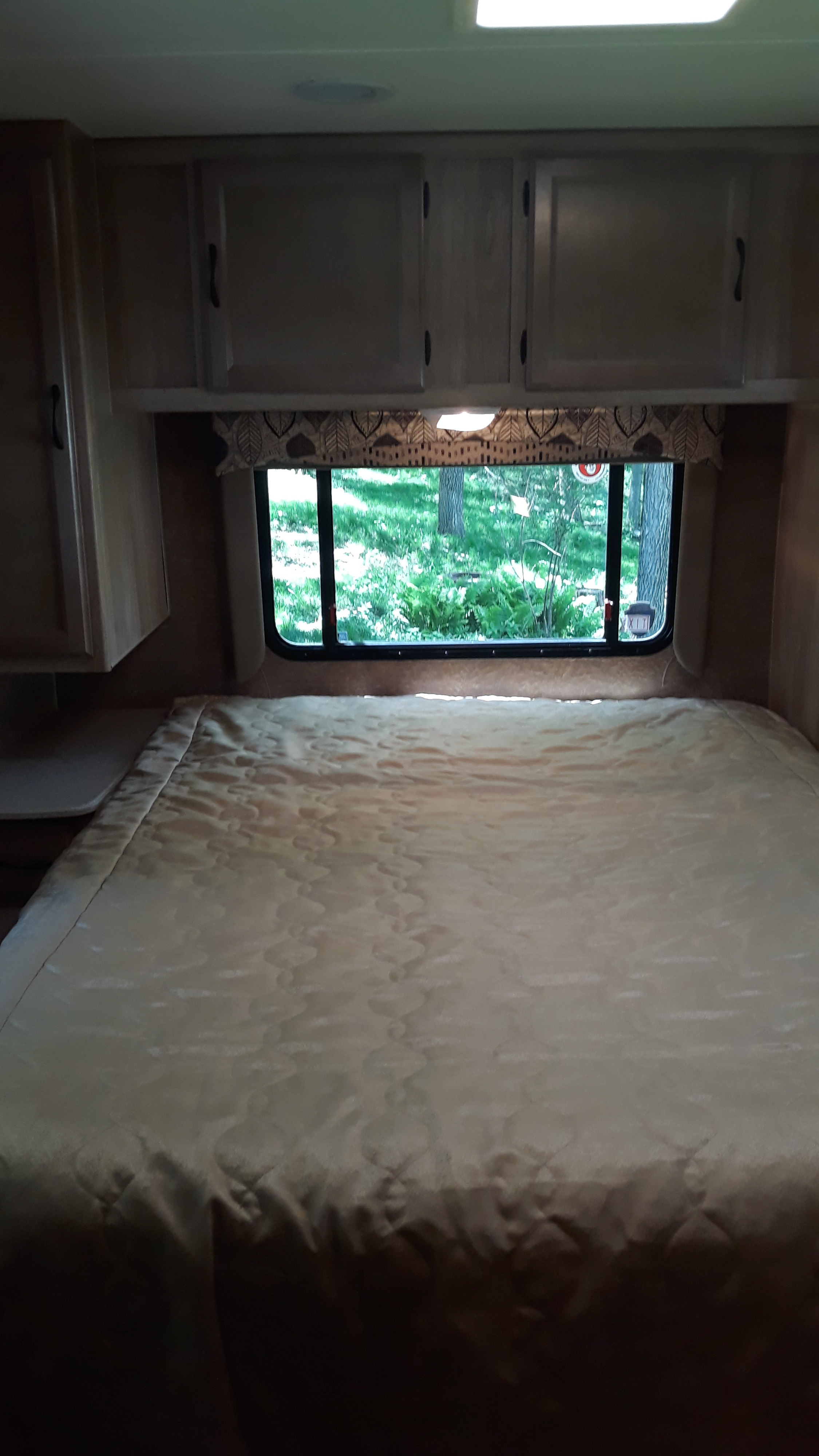RV rental bedroom with a comfy quilted bed, overhead cabinets, and a scenic window view.. Forest River Coachmen Freelander 2014