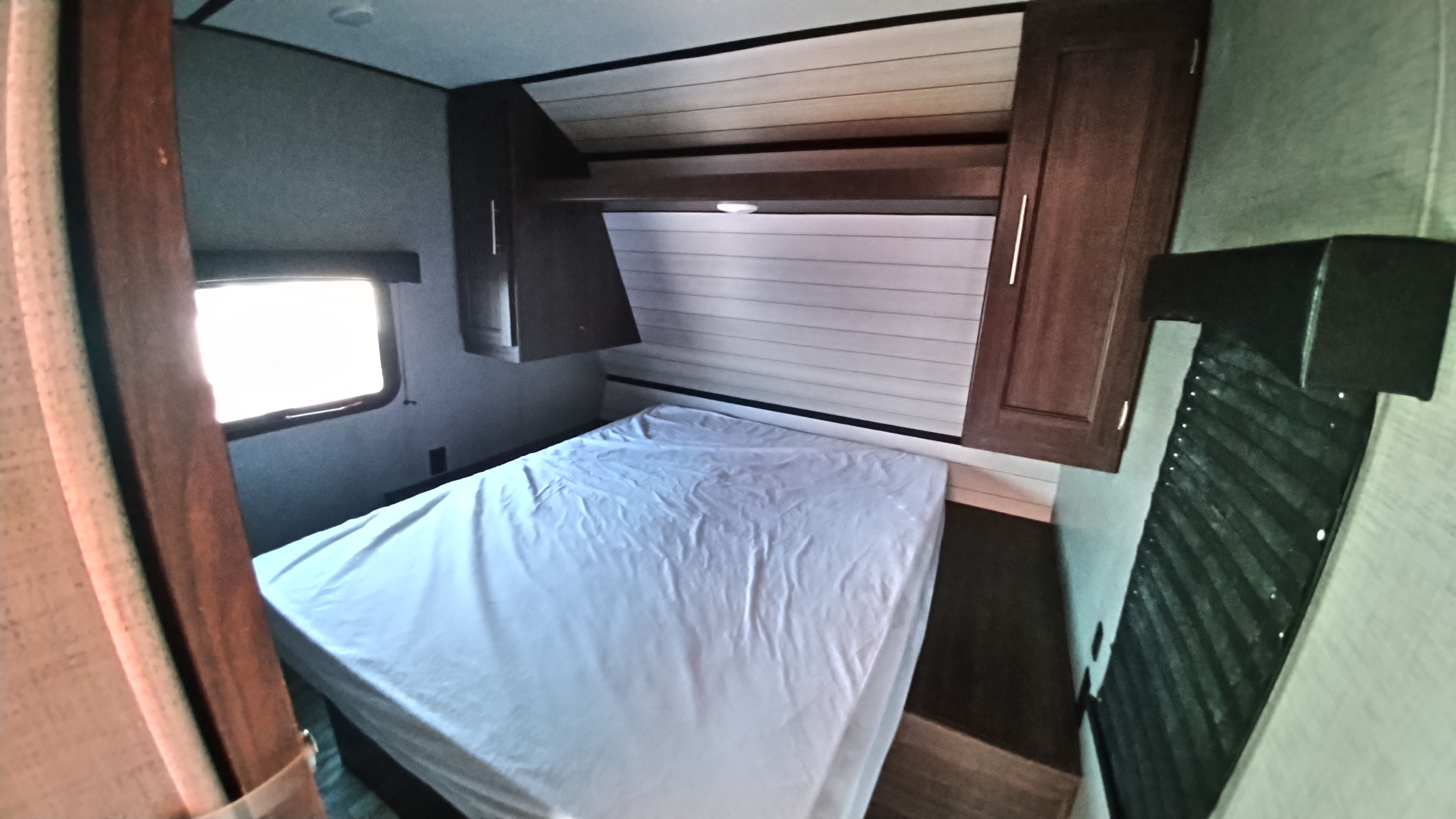 Cozy RV rental bedroom with a comfortable bed, overhead cabinets, and a side window, perfect for your next adventure.. Crossroads Zinger 2019