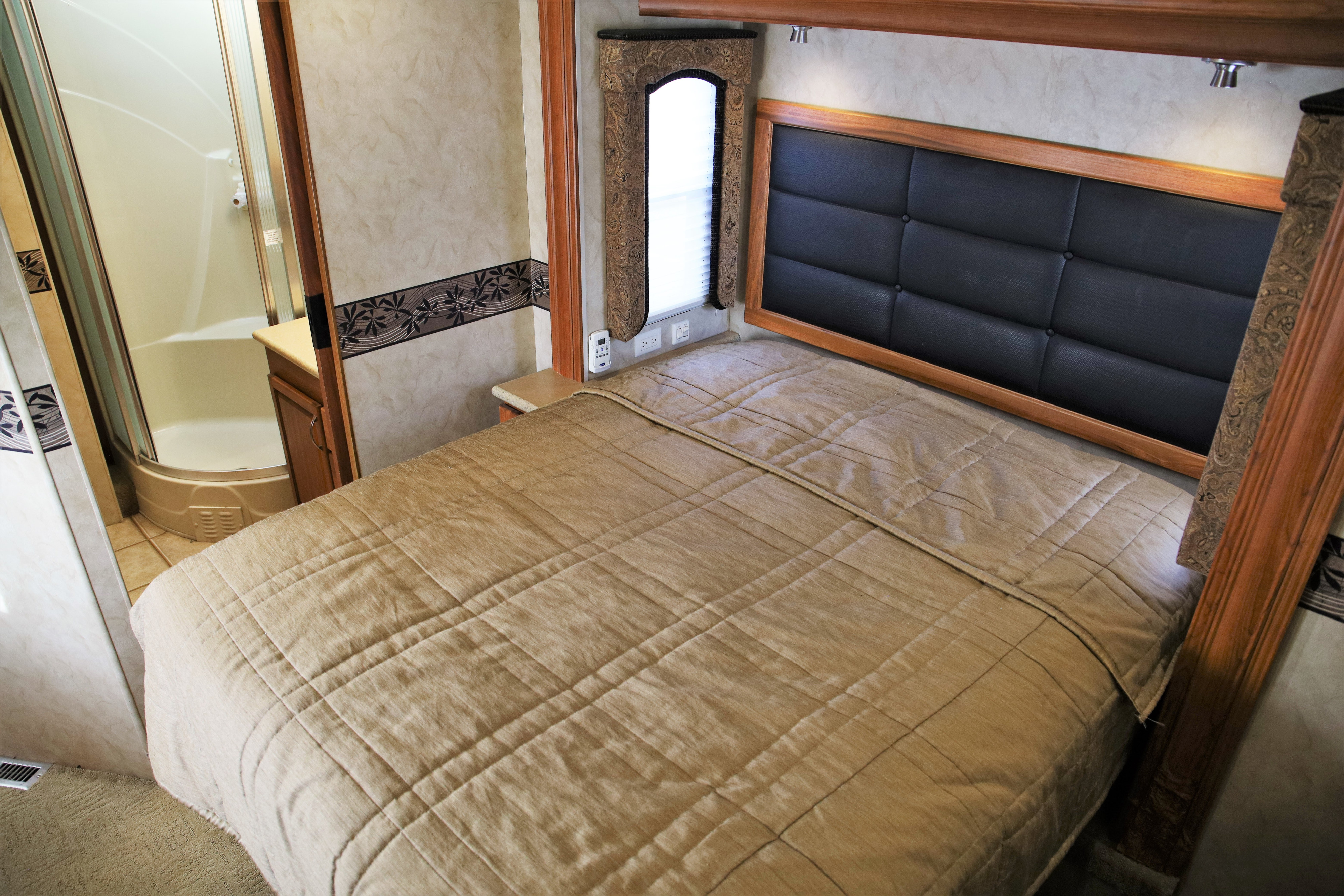 Explore this RV rental's cozy bedroom, featuring a comfy bed with a padded headboard, window, and adjacent shower stall.. Monaco La Palma 2009