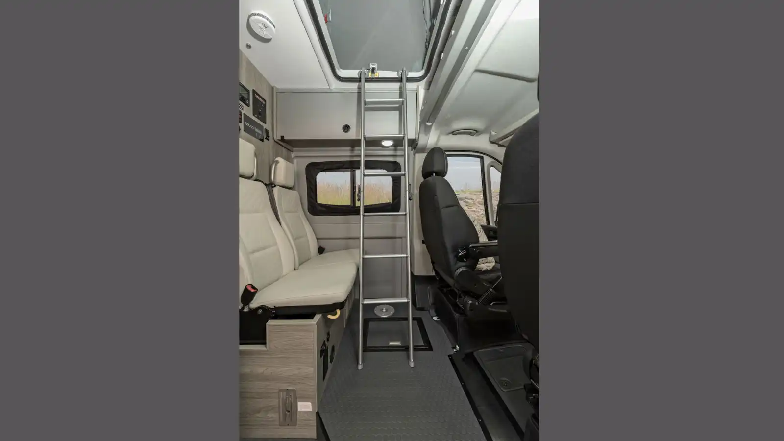 Interior of a modern RV rental camper van, showing a ladder to an overhead bunk, bench seating, and driver's cab.. Winnebago Solis 59PX 2022