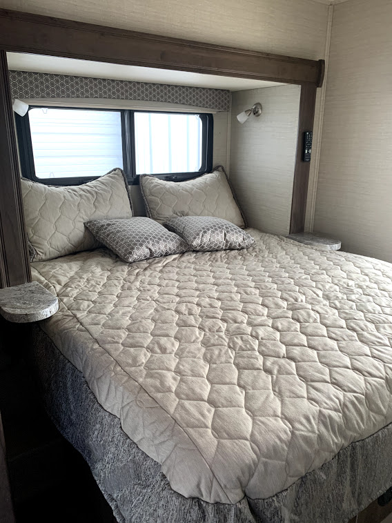 Cozy RV rental bedroom featuring a large bed with quilted bedding, pillows, and windows. Ideal for comfortable travel.. Jayco Greyhawk 2020