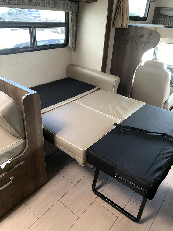 Inside an RV rental, a beige and black convertible sofa bed extends, providing versatile sleeping space for travel.. Jayco Greyhawk 2020