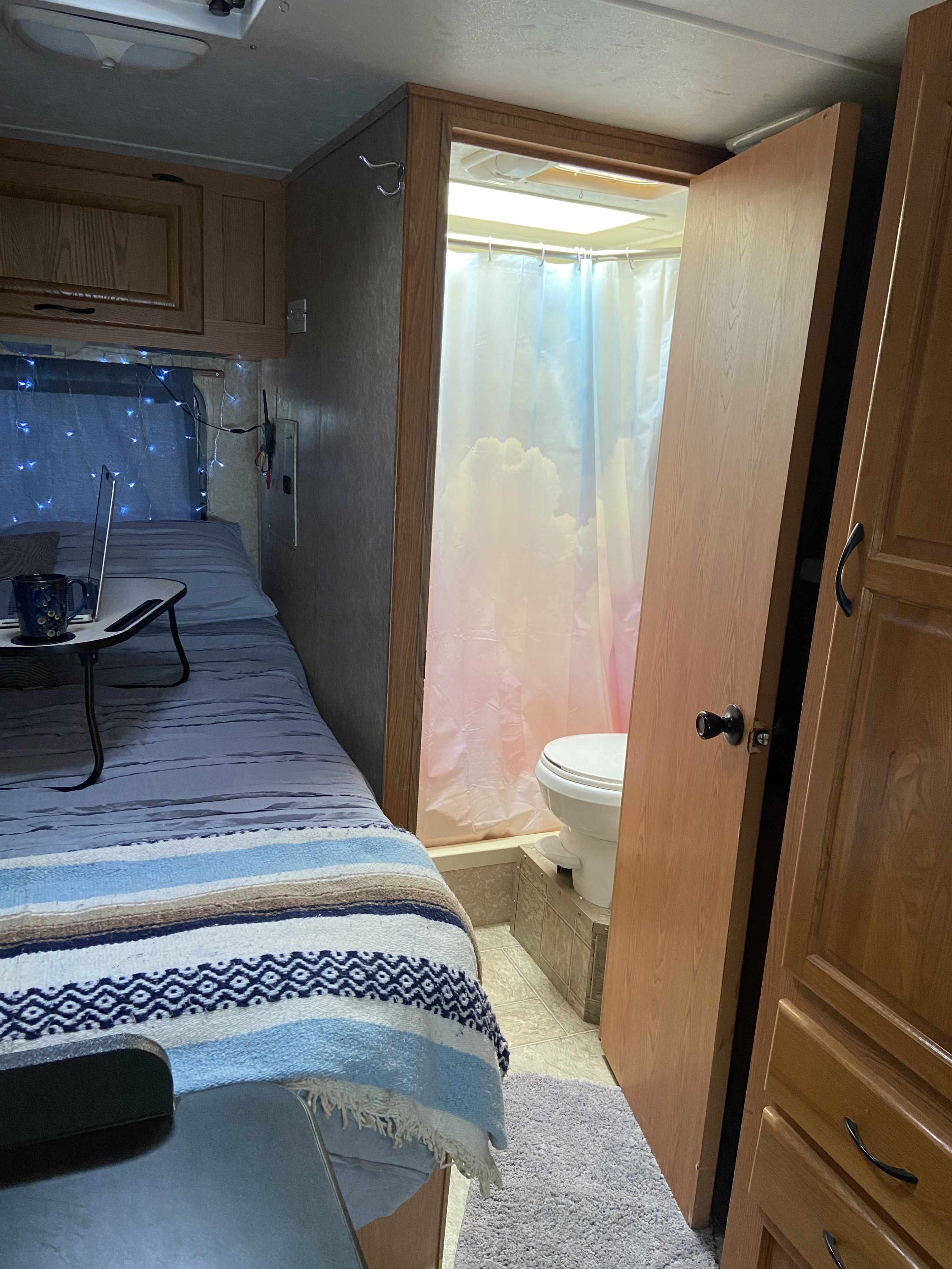 Cozy RV rental interior: a compact bedroom with blue lights and laptop, and an adjacent bathroom with a cloud shower curtain.. Thor Motor Coach Four Winds Majestic 2009