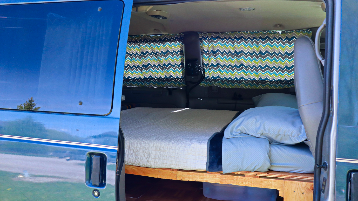 Inside a blue camper van: a cozy bed, chevron curtains, and storage beneath. Ideal for your next RV rental road trip.. Chevrolet Other 2003