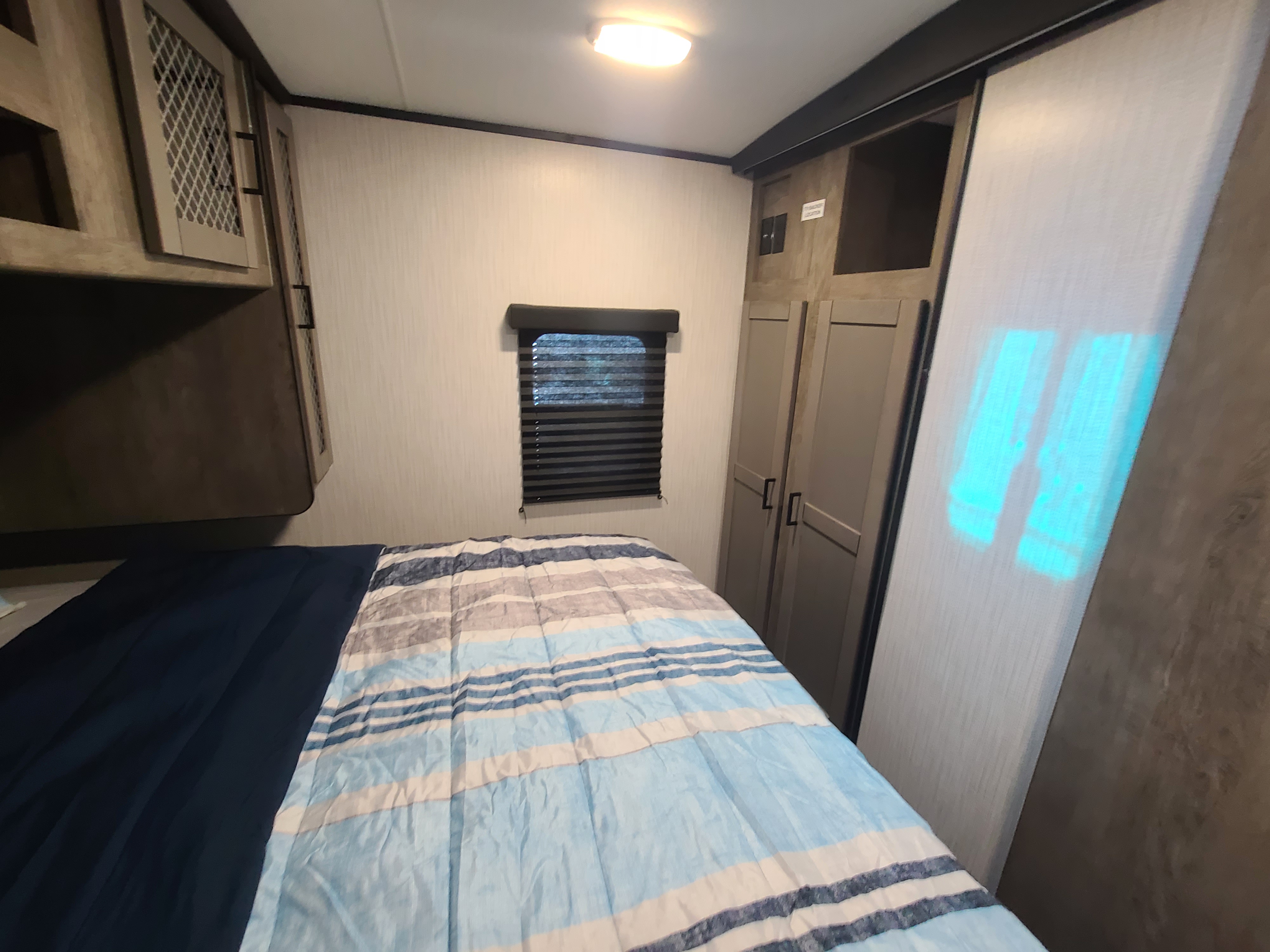 Cozy RV rental bedroom with striped bed, overhead cabinets, window, and built-in wardrobe/storage.. Heartland North Trail 24DBS 2021