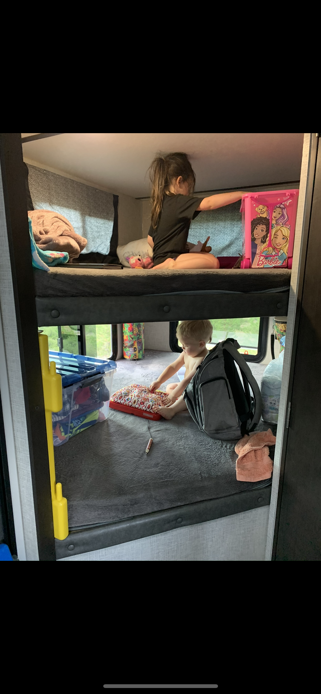 Kids enjoying their RV rental bunk beds. An older girl on top, a toddler playing with toys below, amidst travel comforts.. Work and Play Work and Play Trailer 2020