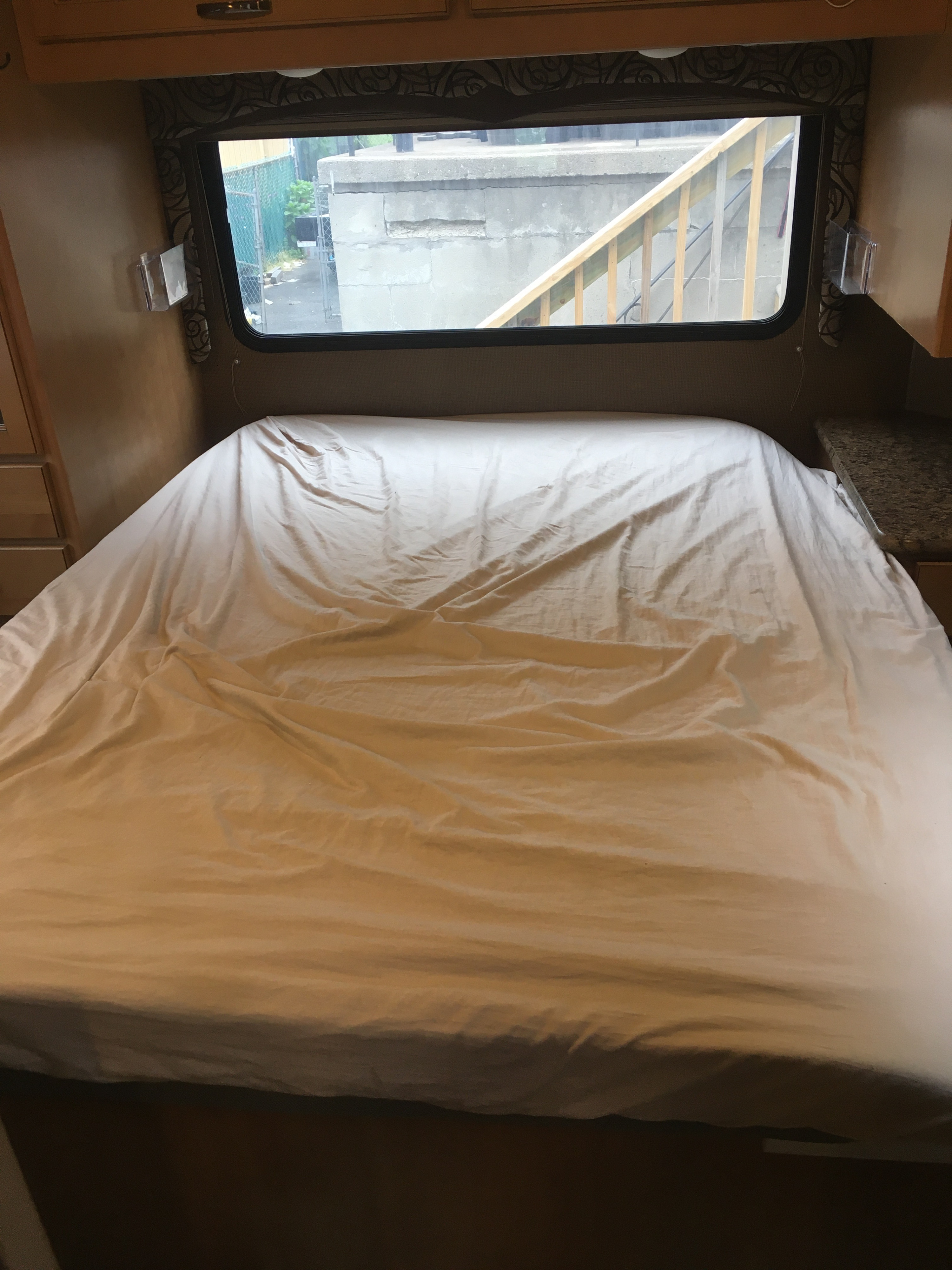 RV rental: The interior shows a sheet-covered bed below a window with an urban view, offering a cozy sleeping space.. Thor Motor Coach Four Winds 2017