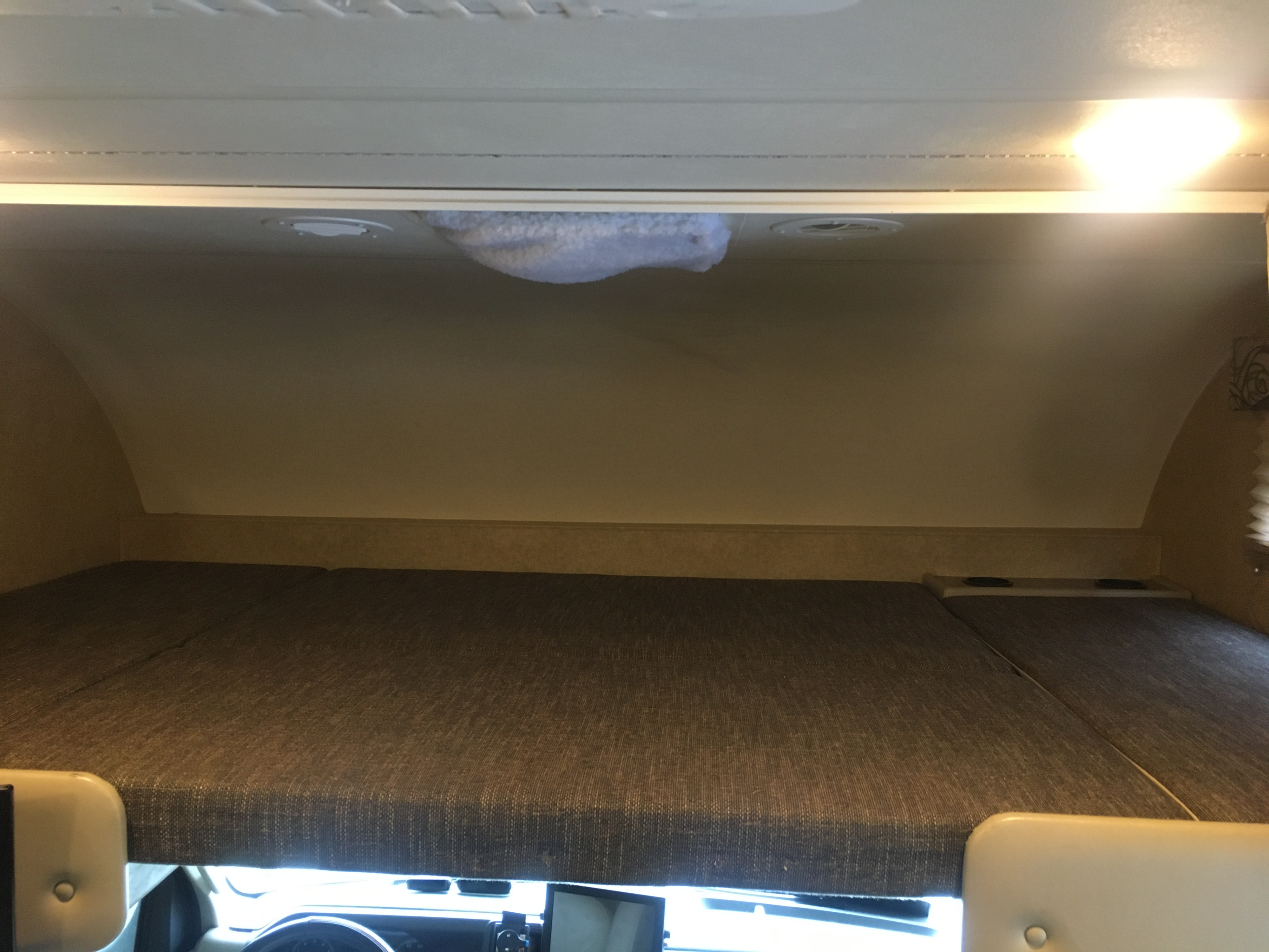 View of a cab-over bunk bed in an RV rental. Features a mattress, embedded cup holders, and overhead lighting for a comfortable sleeping area.. Thor Motor Coach Four Winds 2017