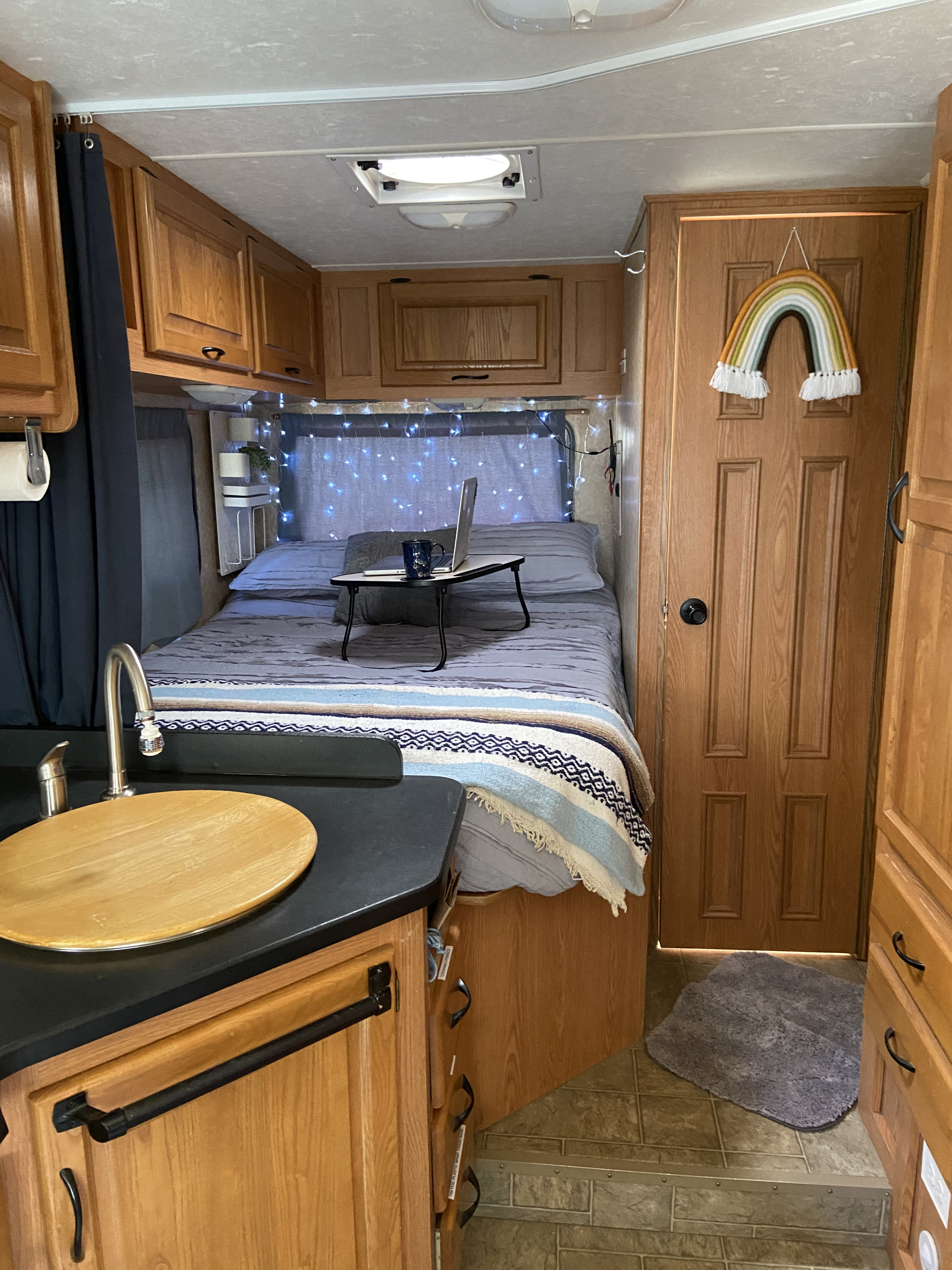 Warm RV rental interior features a cozy bed with a laptop, fairy lights, and a functional kitchenette.. Thor Motor Coach Four Winds Majestic 2009