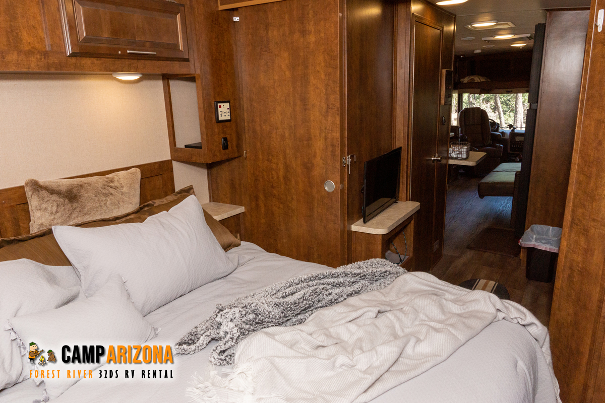 Spacious RV interior: a comfortable bedroom with light grey bedding, rich wood cabinets, and access to the living area. Perfect rv rental.. Forest River FR3 32 DS 2016