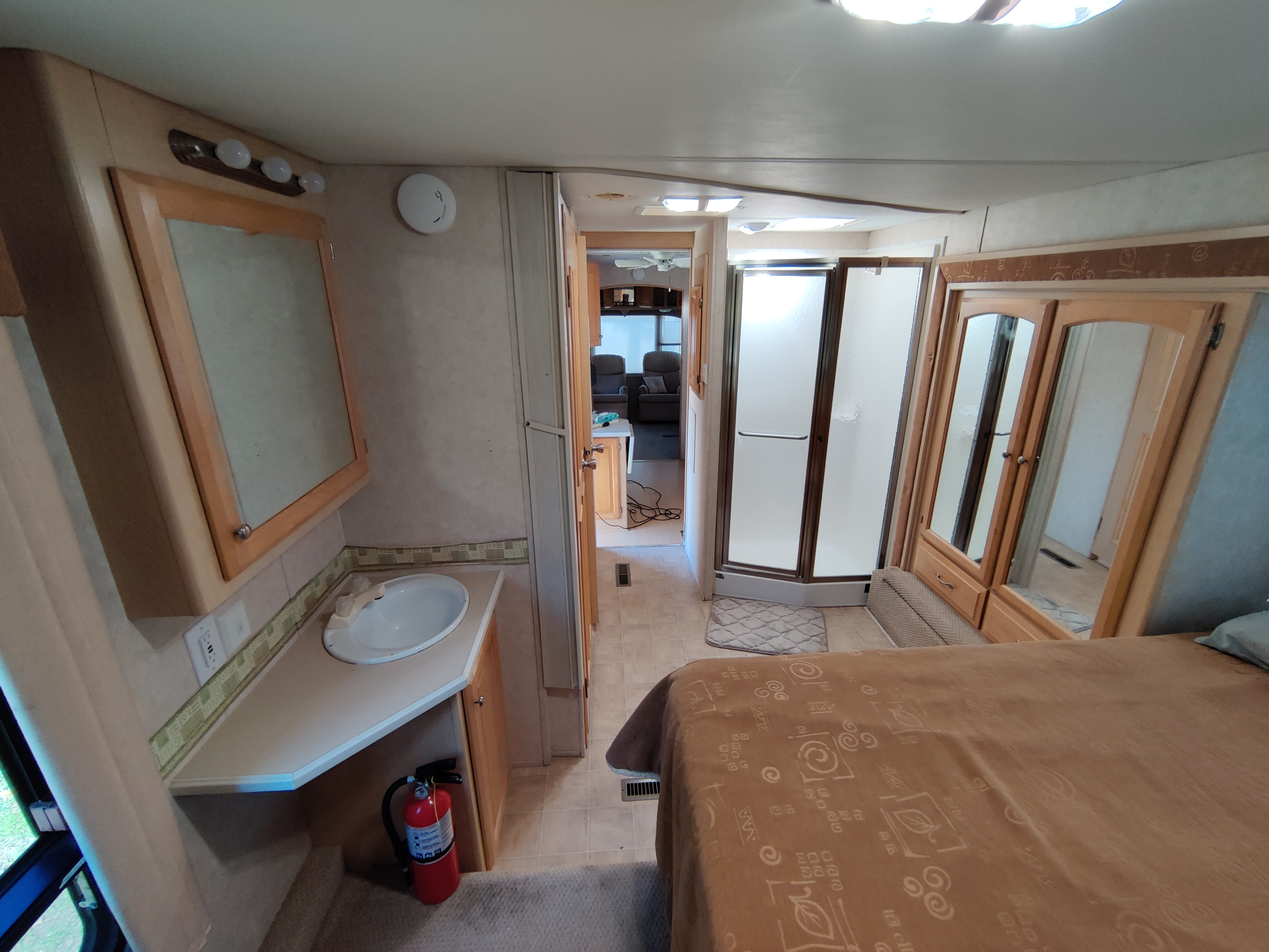 RV rental interior: bedroom, bath vanity with sink, shower stall, and mirrored closet visible. Fire extinguisher below vanity.. Carriage Cameo 2004