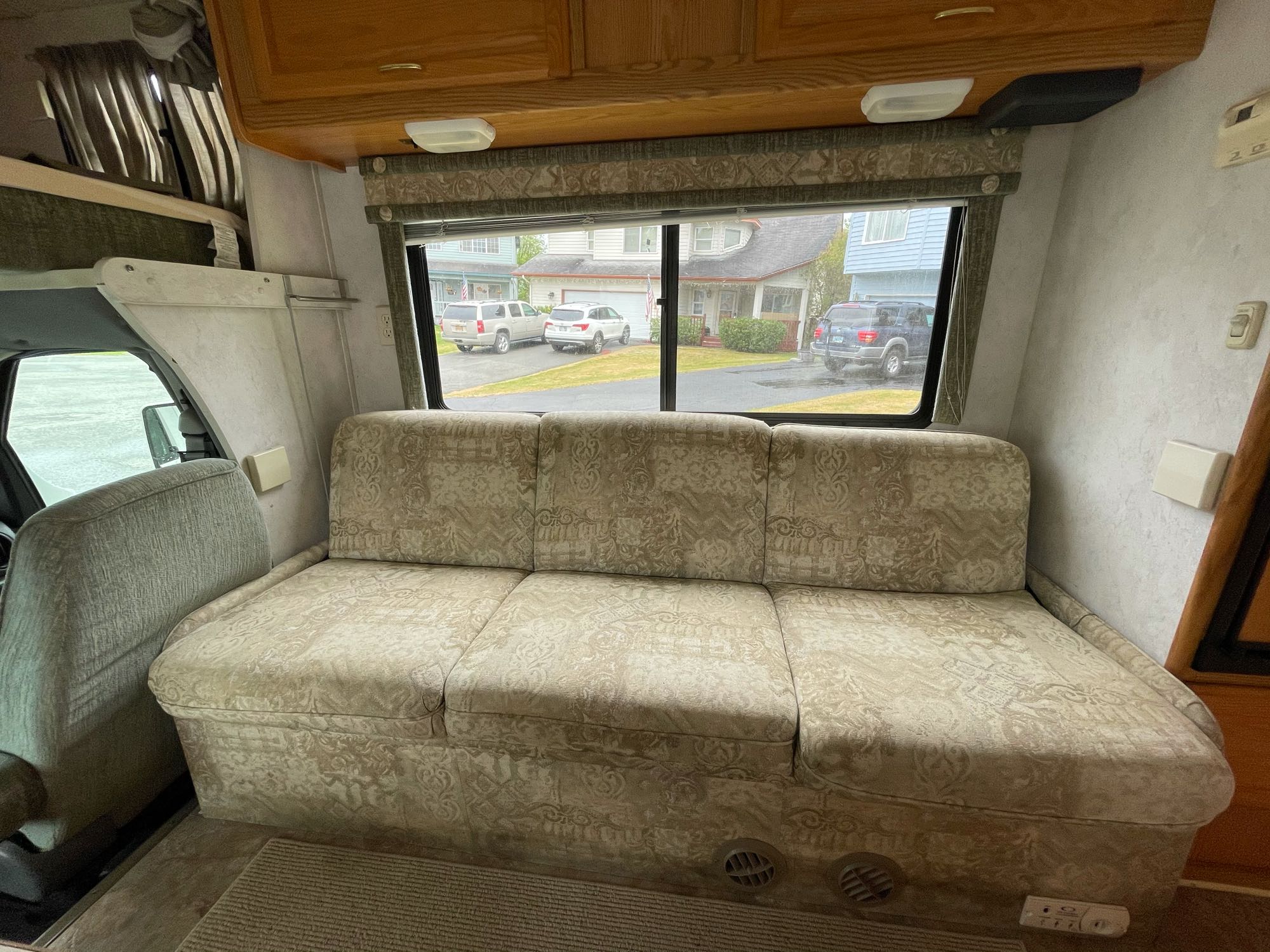Inside an **rv rental**: a comfortable sofa, overhead cabinets, and a window looking out onto a residential street.. Winnebago Chalet 2004