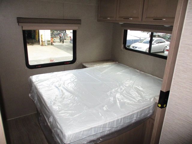 RV rental bedroom interior: bed with new plastic-wrapped mattress, overhead cabinets, and windows.. Thor Motor Coach Daybreak 2021