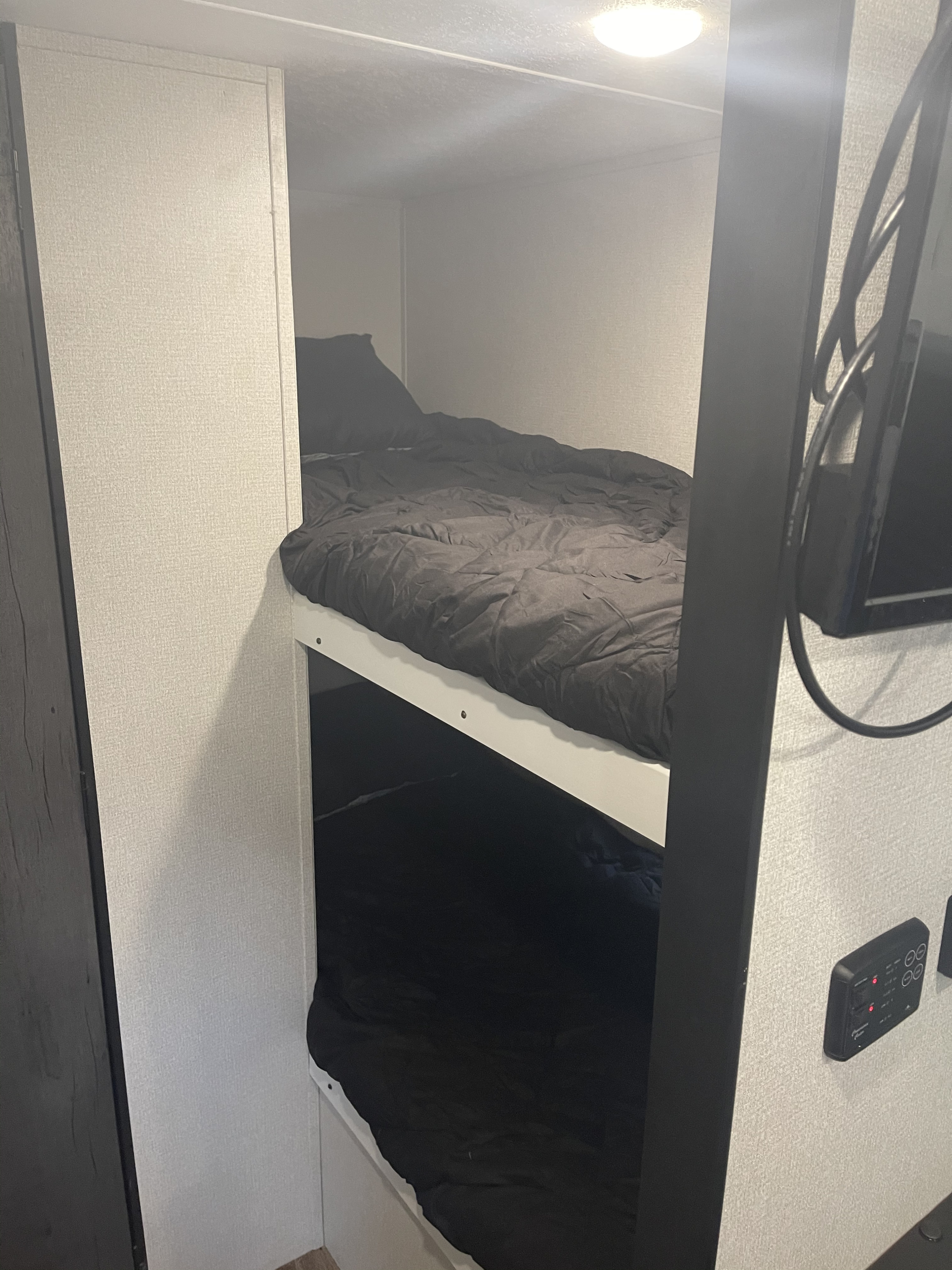 Compact RV rental interior featuring two bunk beds with black bedding, a ceiling light, and wall-mounted controls and TV.. keystone Hideout 2021