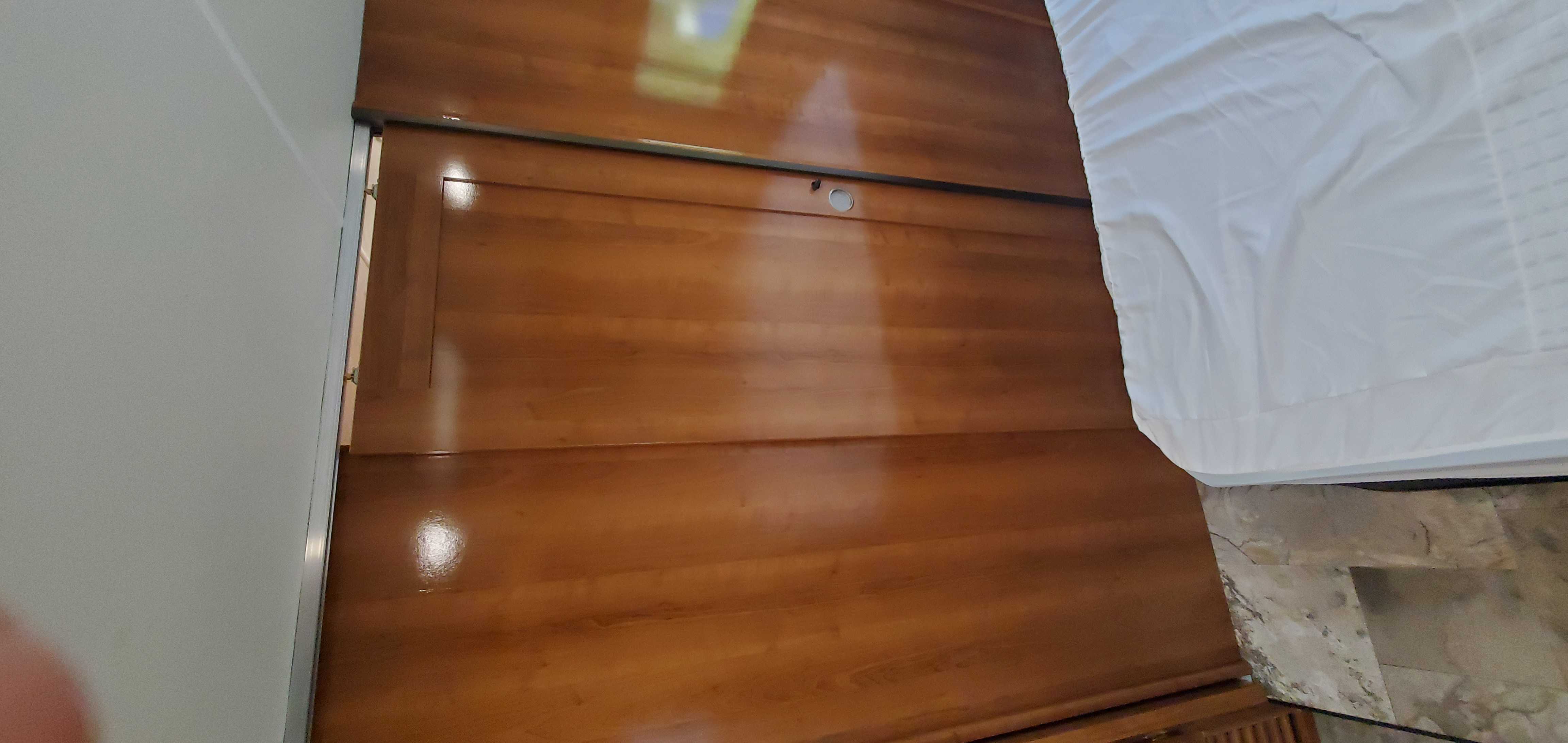 RV rental bedroom: a bed with white linens borders a wall of glossy wooden panels and storage. Compact and neat.. Coachmen Leprechaun 2019