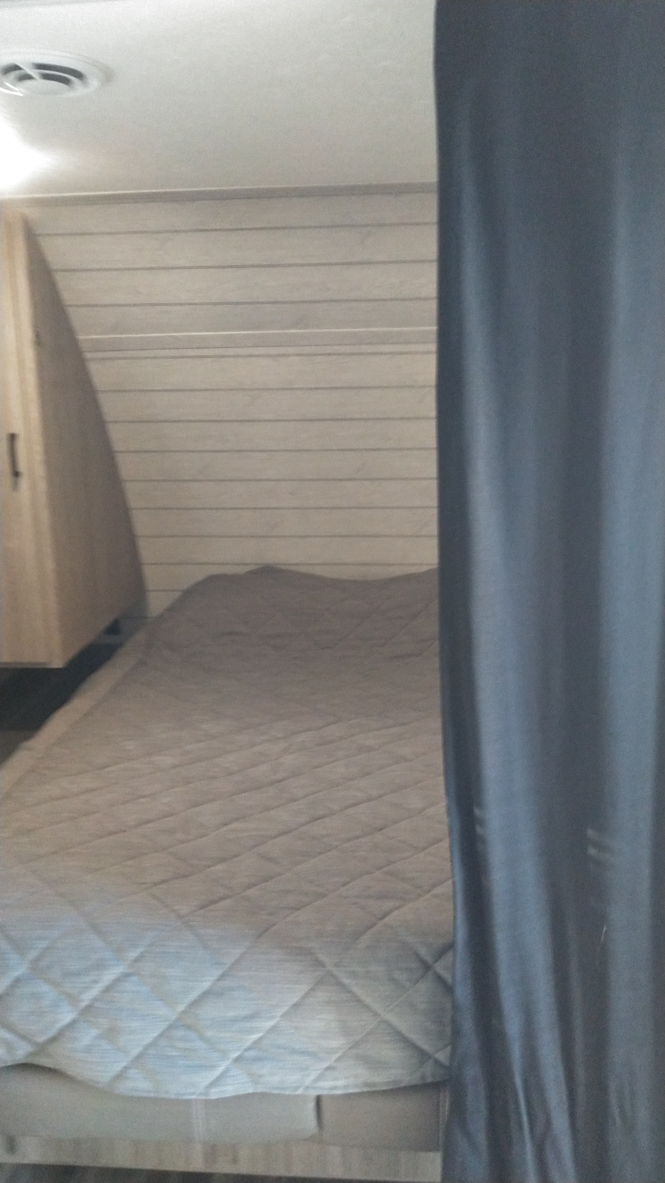 Compact bedroom in an RV rental, featuring a comfortable bed, wood-paneled wall, and privacy curtain.. Keystone RV Passport SL 2021