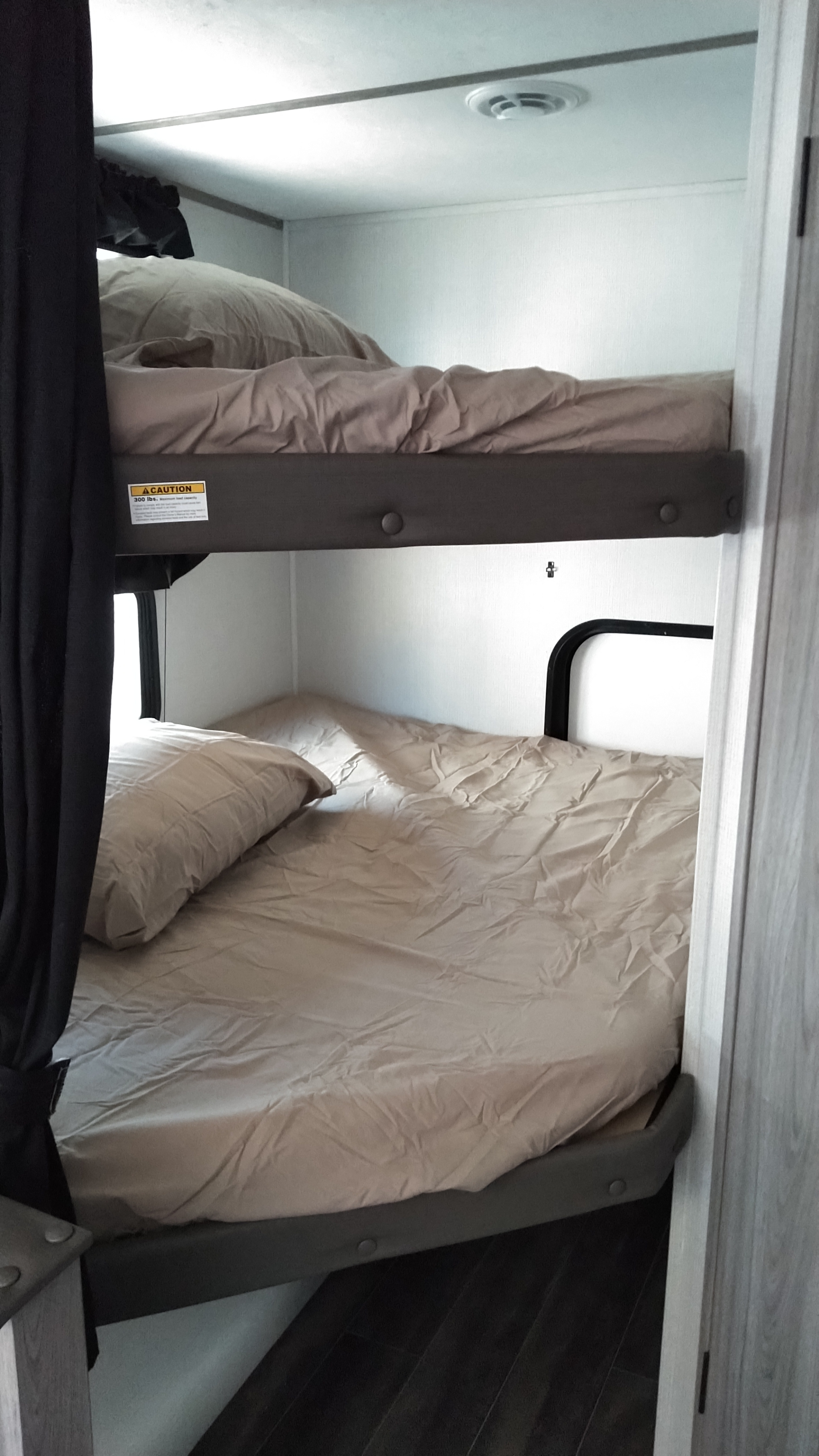 Cozy RV rental bunk beds, with tan bedding and a 300lb capacity top bunk. Ideal compact sleeping area for families.. Keystone RV Passport SL 2021