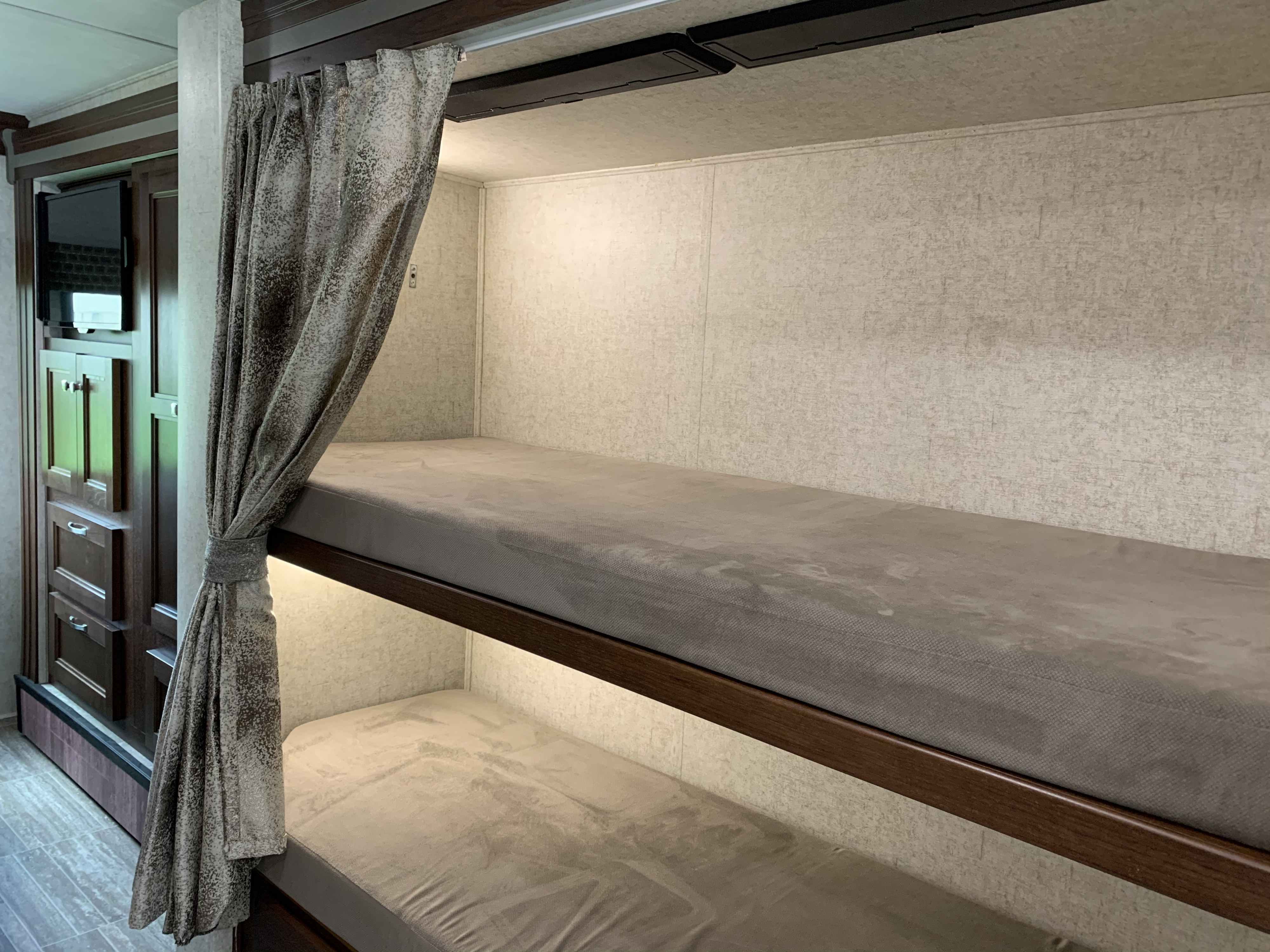Cozy bunk beds in an RV rental, featuring light mattresses, a textured privacy curtain, and storage cabinetry.. Forest River Sunseeker 2019