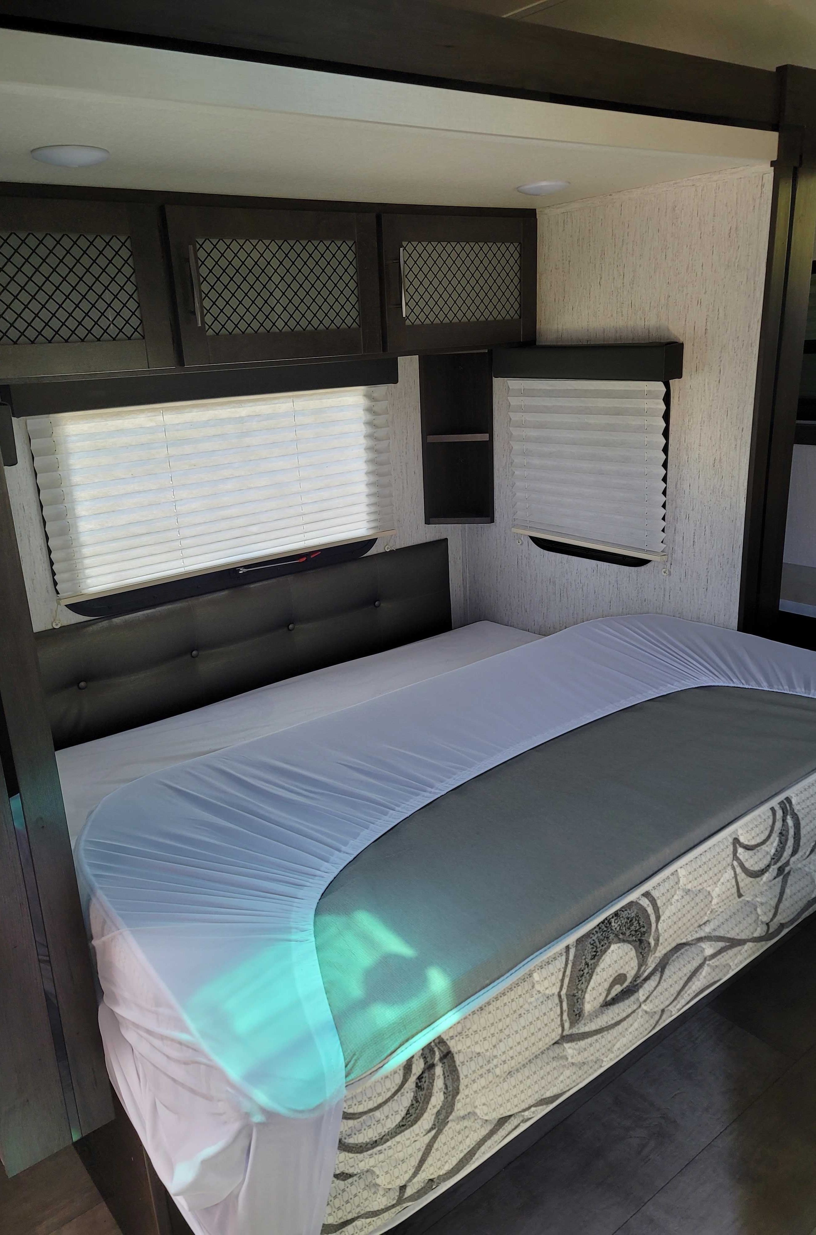 Spacious RV rental bedroom featuring a queen bed with a white fitted sheet, built-in dark cabinets, and pleated window blinds.. Grand Design Momentum 2021