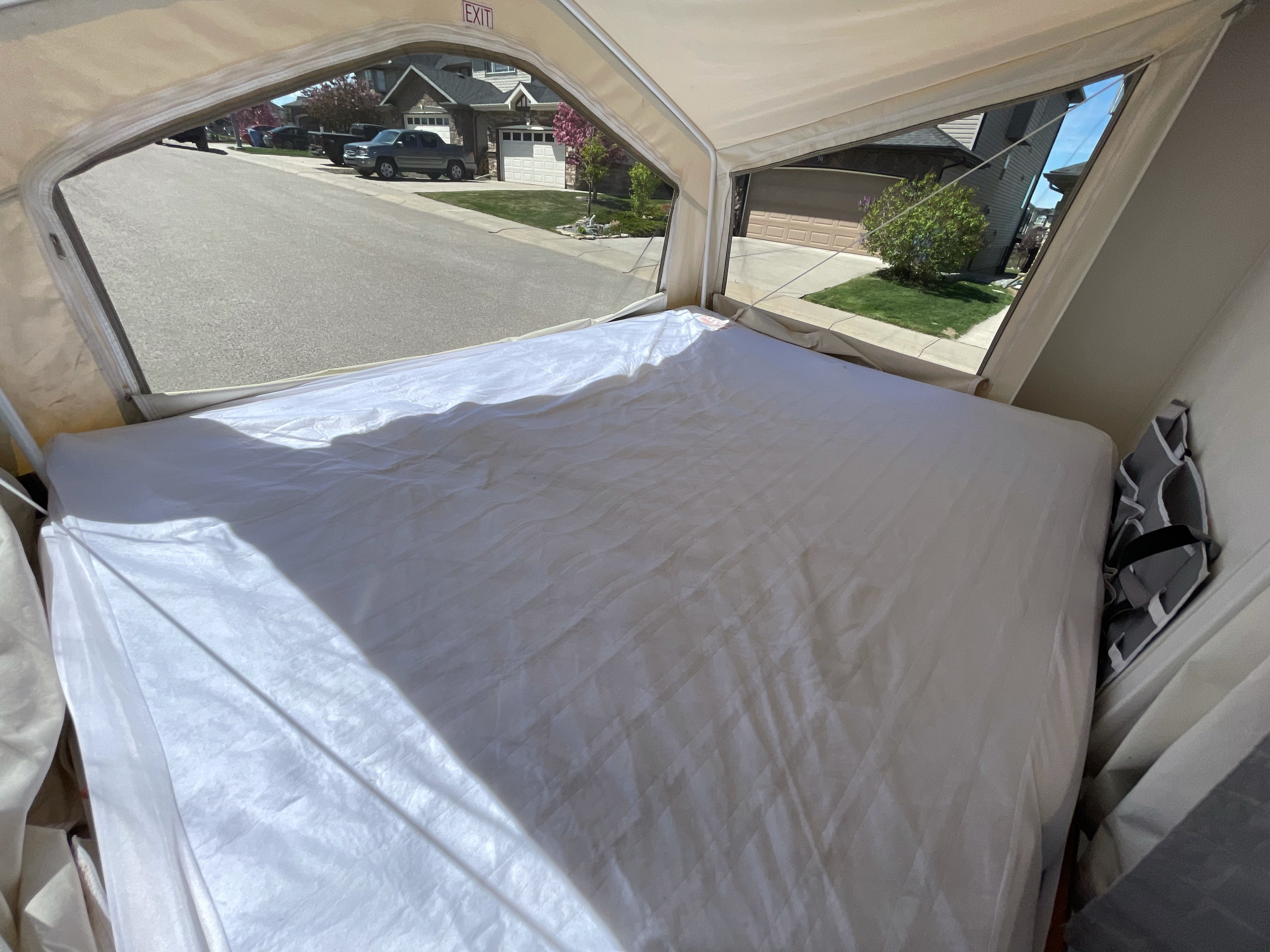Inside an RV rental pop-up camper: a bed with white sheets faces a window overlooking a sunny residential street.. Forest River Rockwood Roo 2010